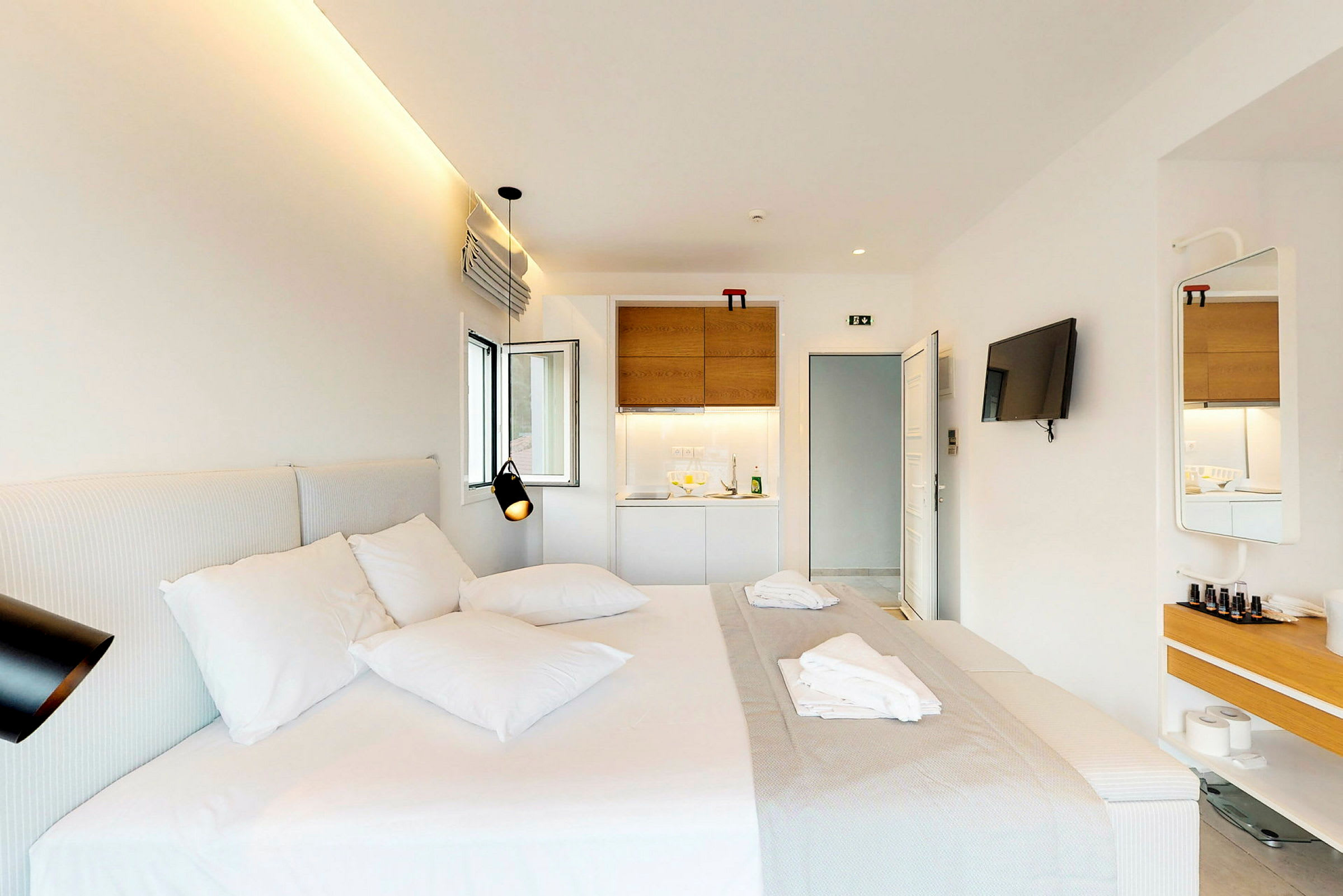Ett modernt hotellrum med en dubbelsäng, en väggmonterad TV och ett litet pentry. (AI-genererad text)