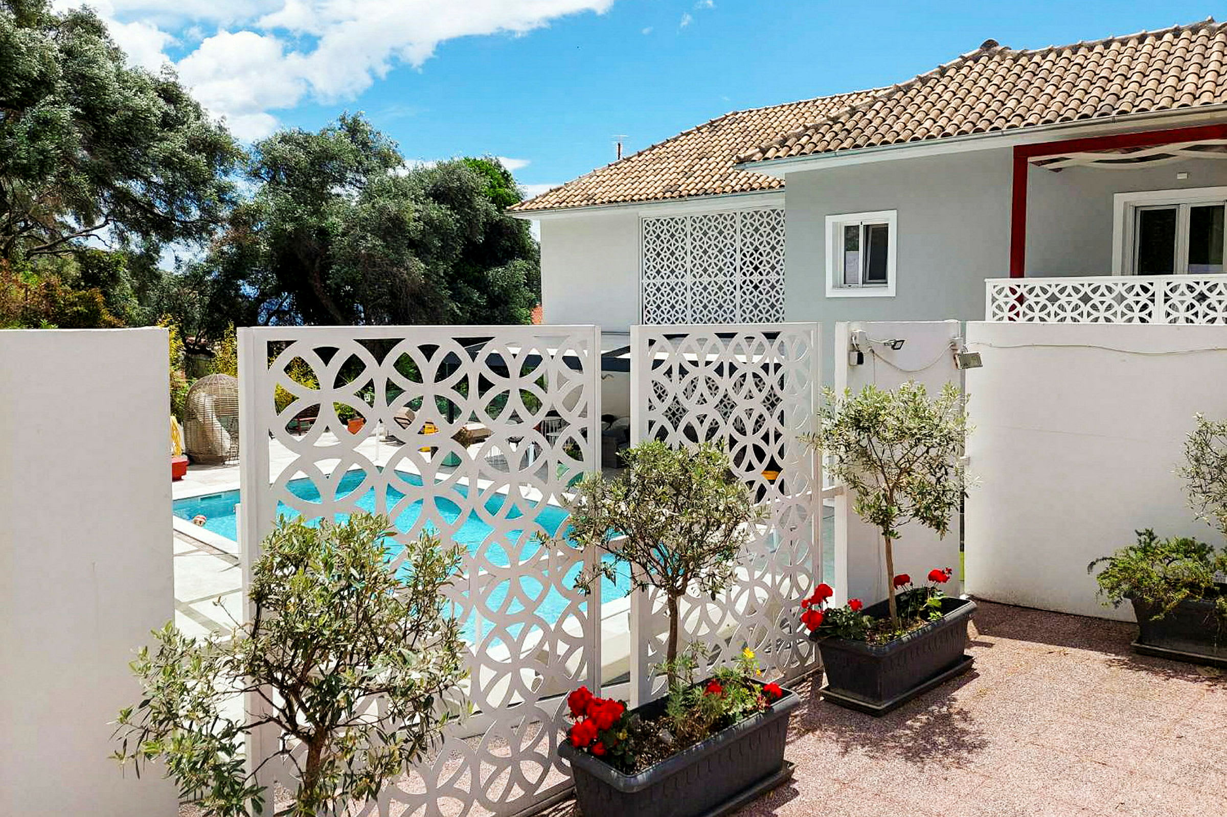 En villa med en pool och dekorativa vita skärmar framför, omgivna av växter och blommor. (AI-genererad text)