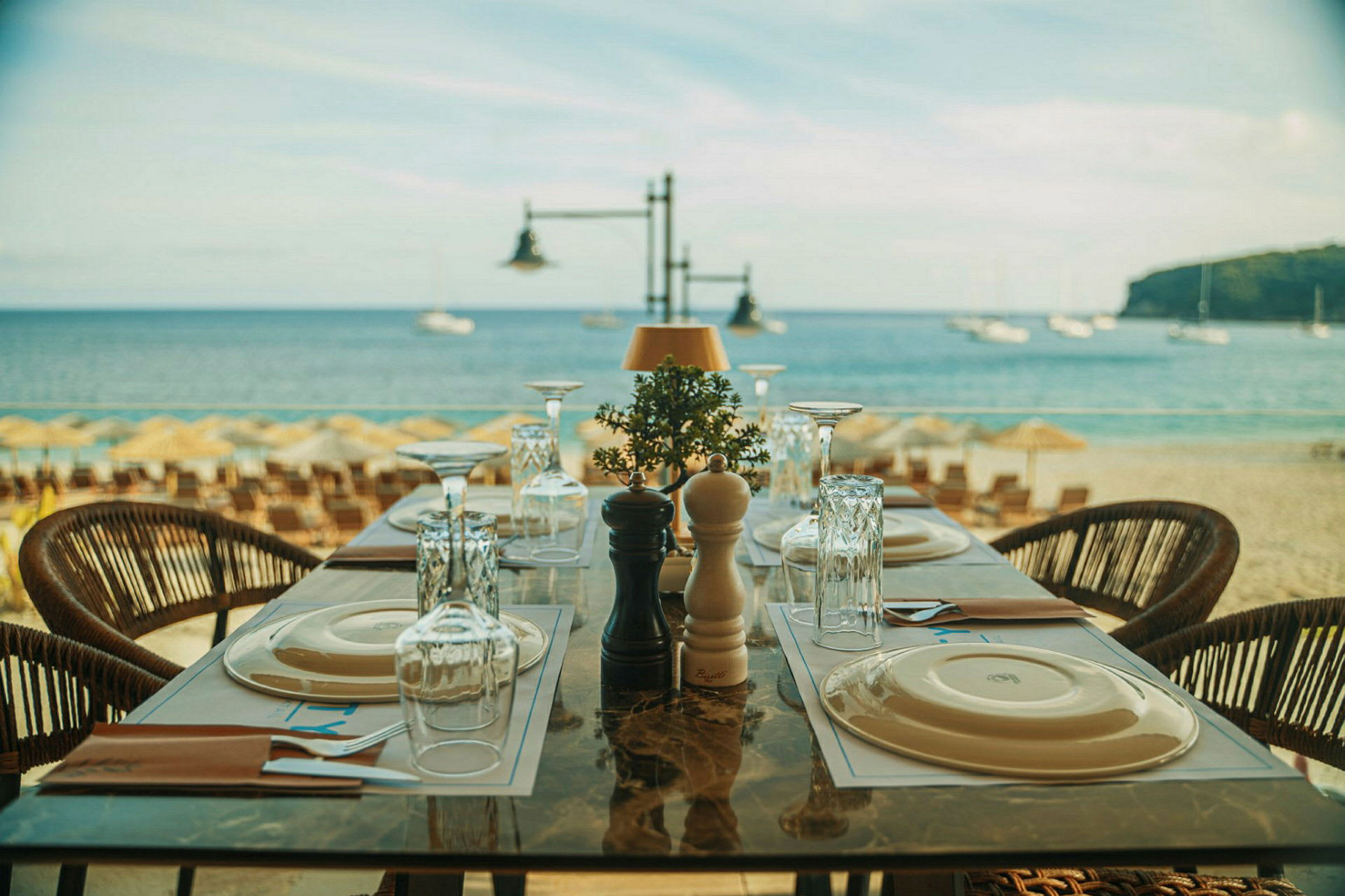 Ett dukat bord på en restaurang vid stranden med stolen havet i bakgrunden. (AI-genererad text)