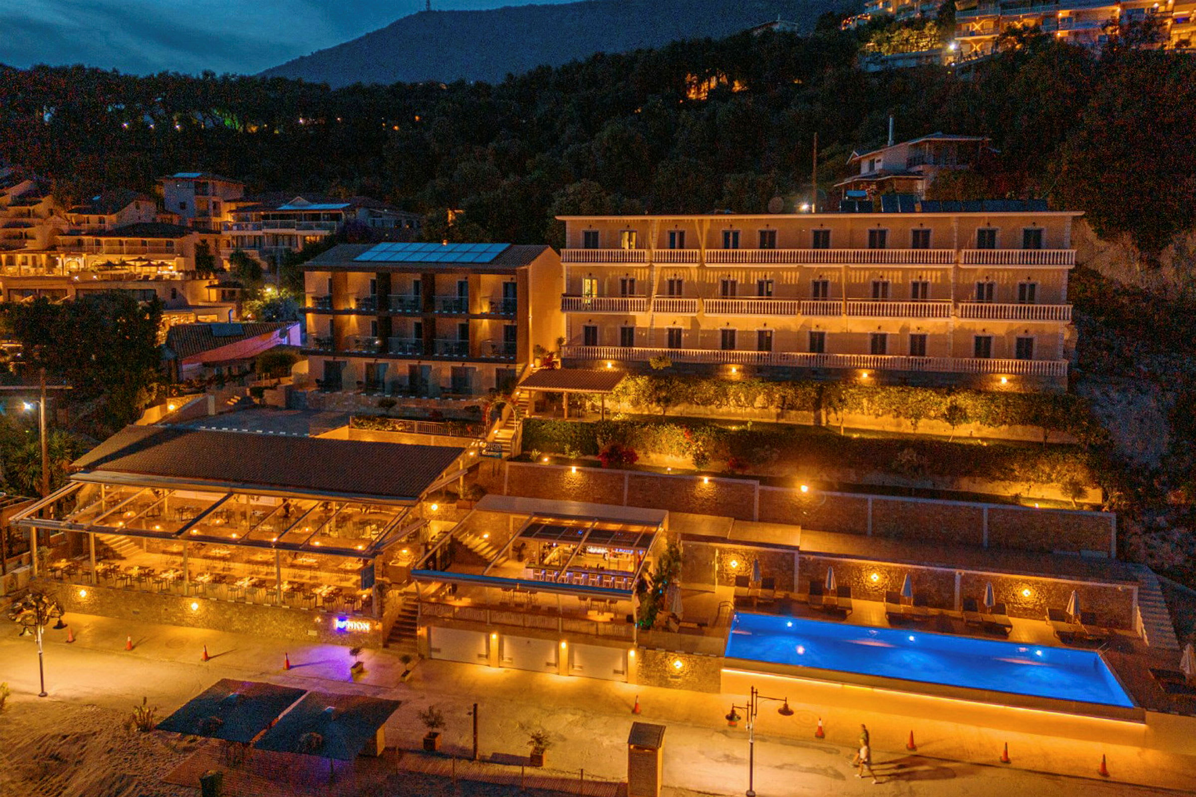 Hotellbyggnad med pool och restaurang belyst på kvällen. (AI-genererad text)