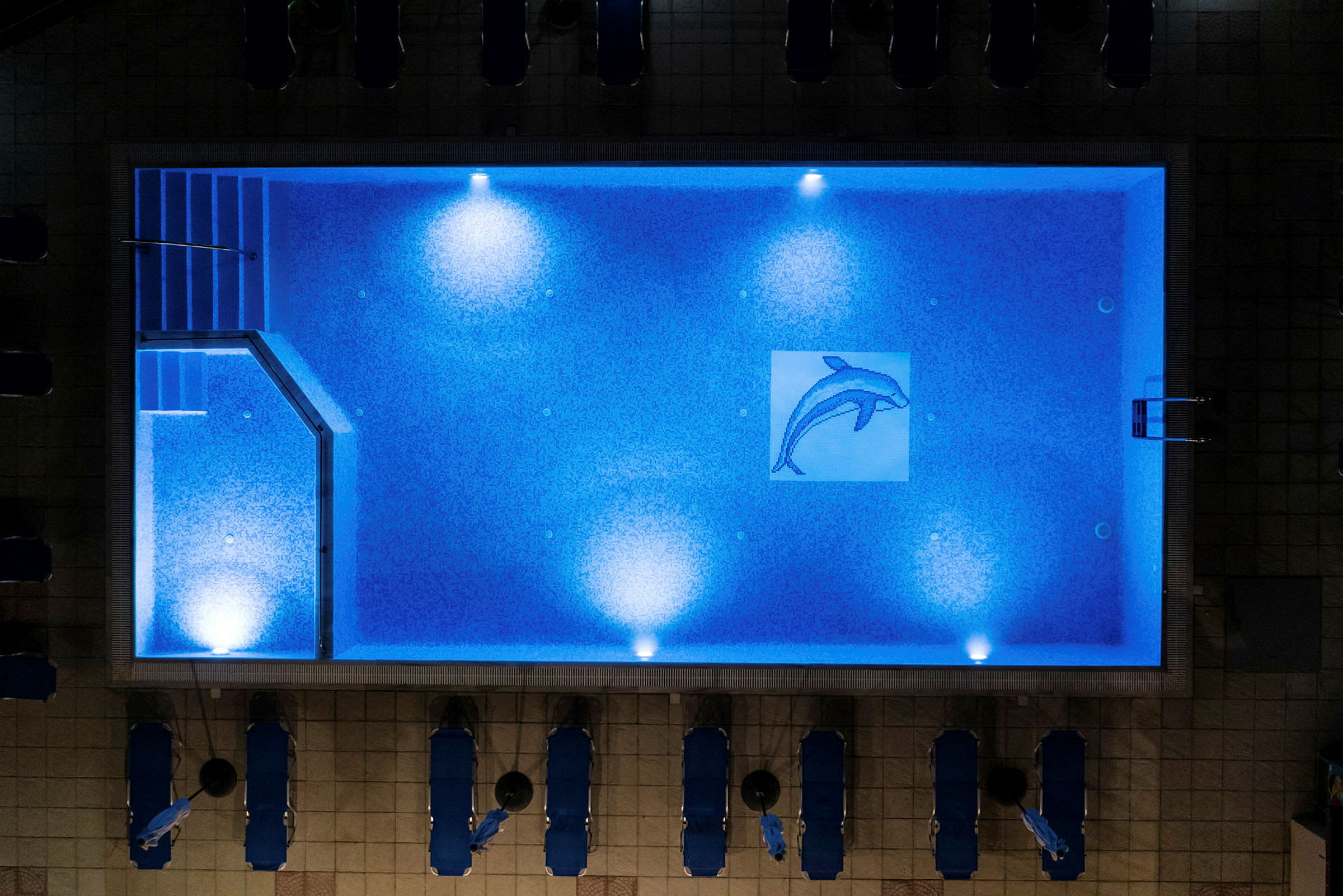 En upplyst simbassäng sedd ovanifrån, med en mosaik av en delfin på botten. (AI-genererad text)
