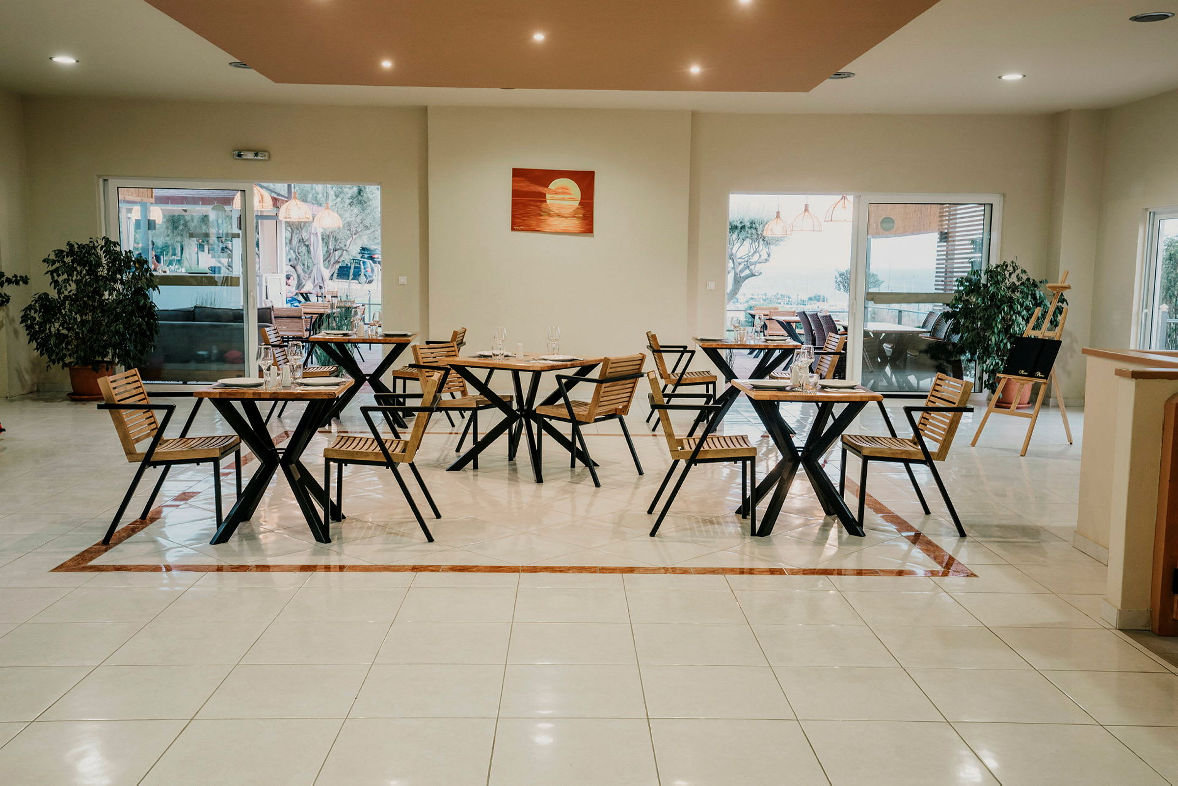 En restaurang med trästolar och bord, stora fönster och inomhusväxt på golvet. (AI-genererad text)