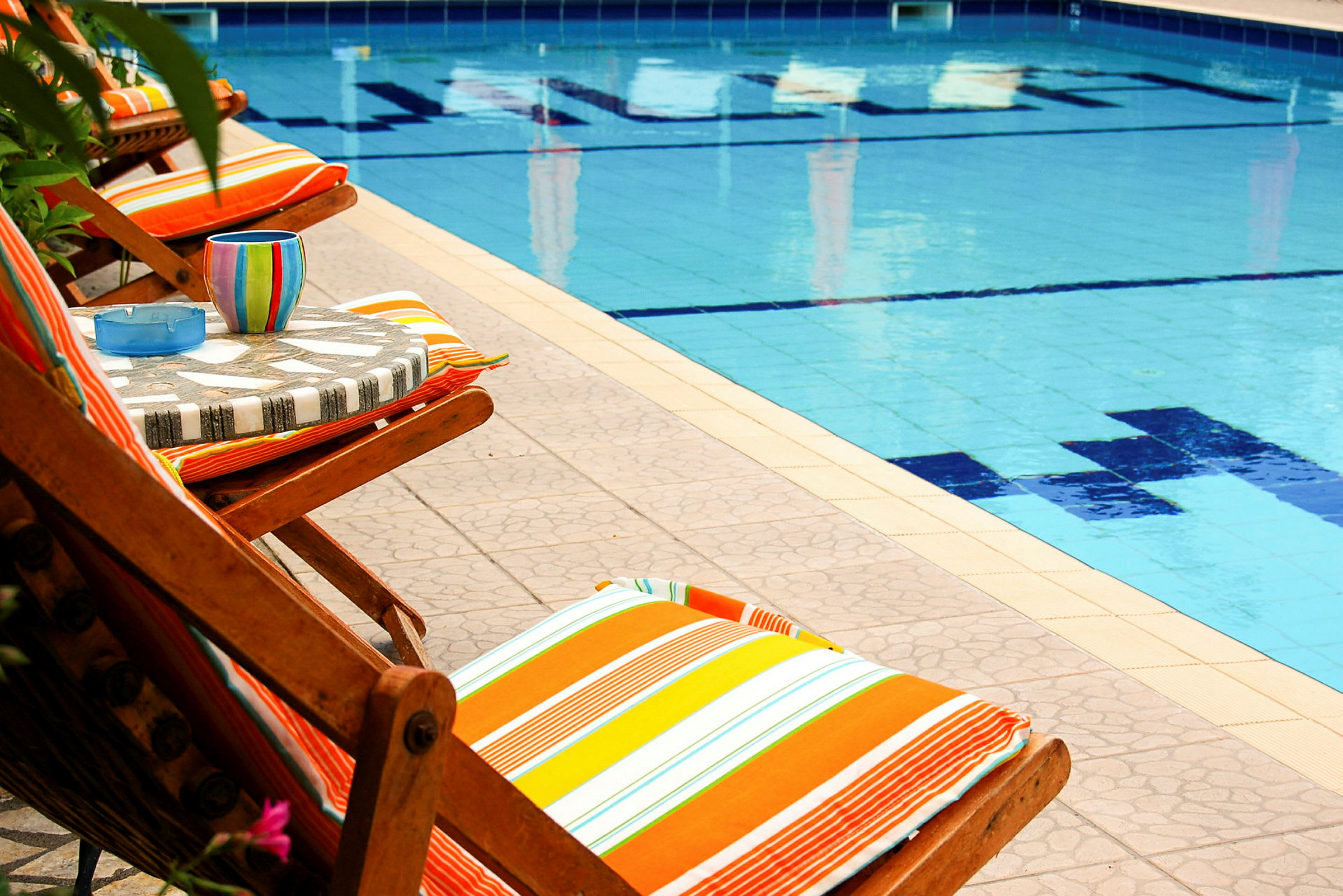 Solsängar med färgglada dynor vid kanten av en swimmingpool. (AI-genererad text)