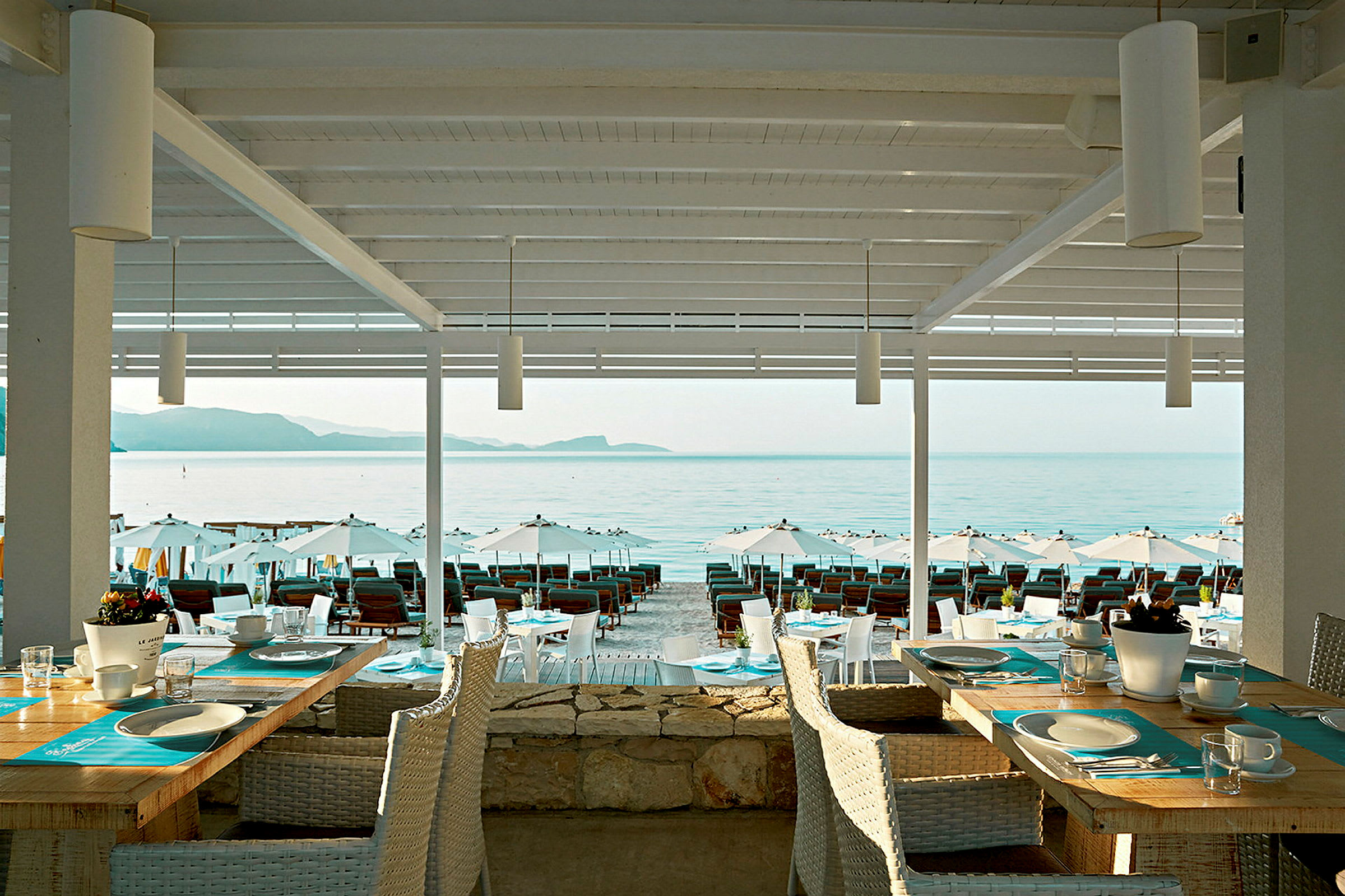 Utsikt från en restaurang med dukade bord mot stranden och havet. (AI-genererad text)