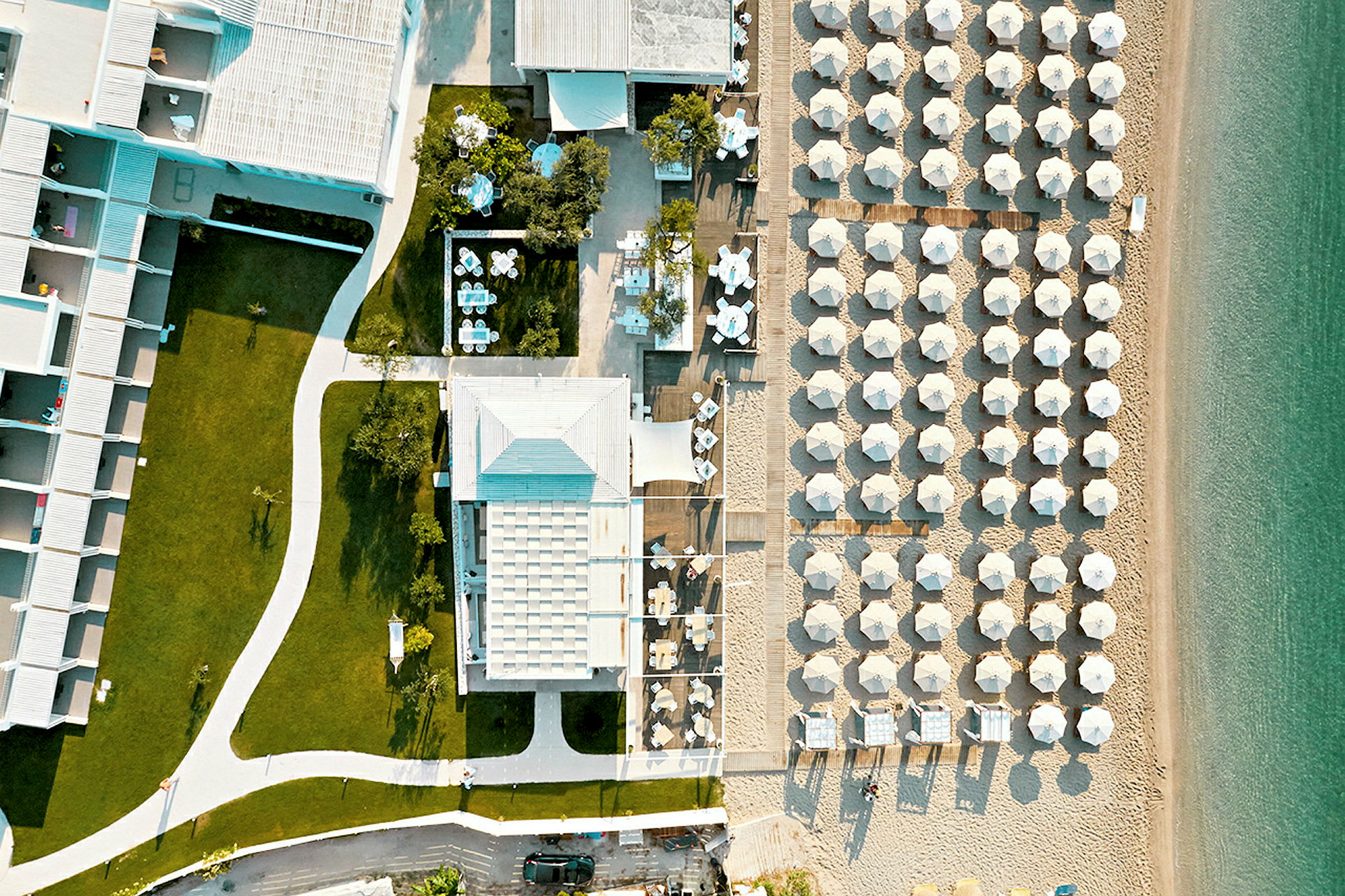 Flygfoto av hotellbyggnad med gräsmattor och strand med parasoller. (AI-genererad text)