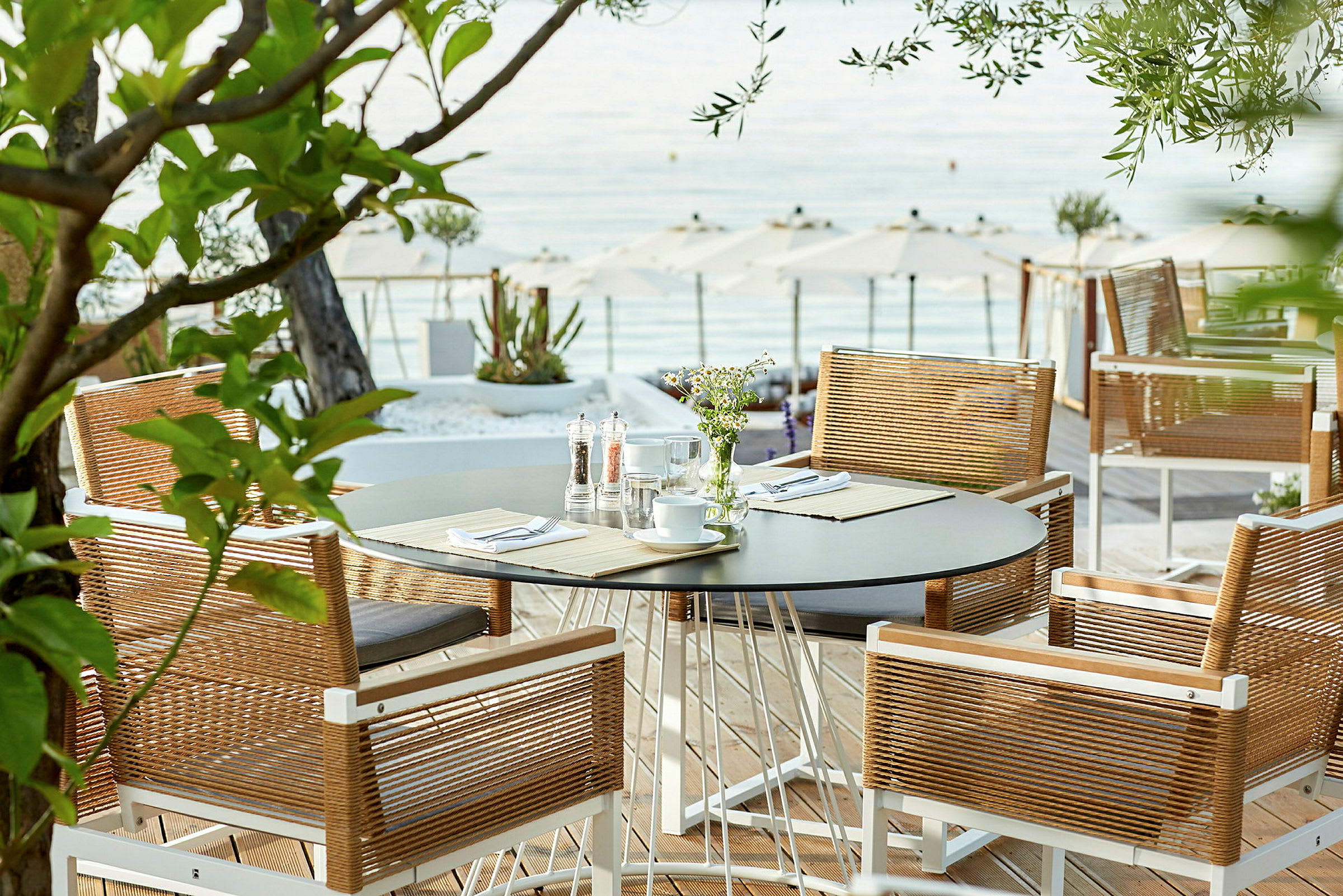 Utsikt mot ett bord med stolar på en terrass nära havet. (AI-genererad text)
