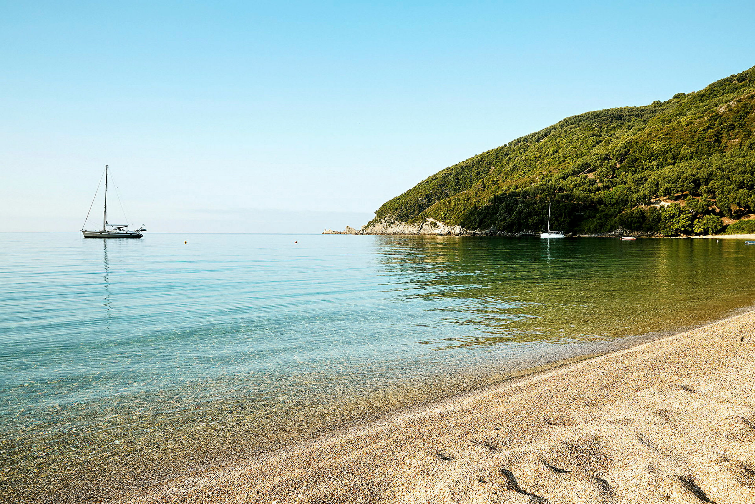 En lugn strand med klart vatten och segelbåtar i fjärran. (AI-genererad text)