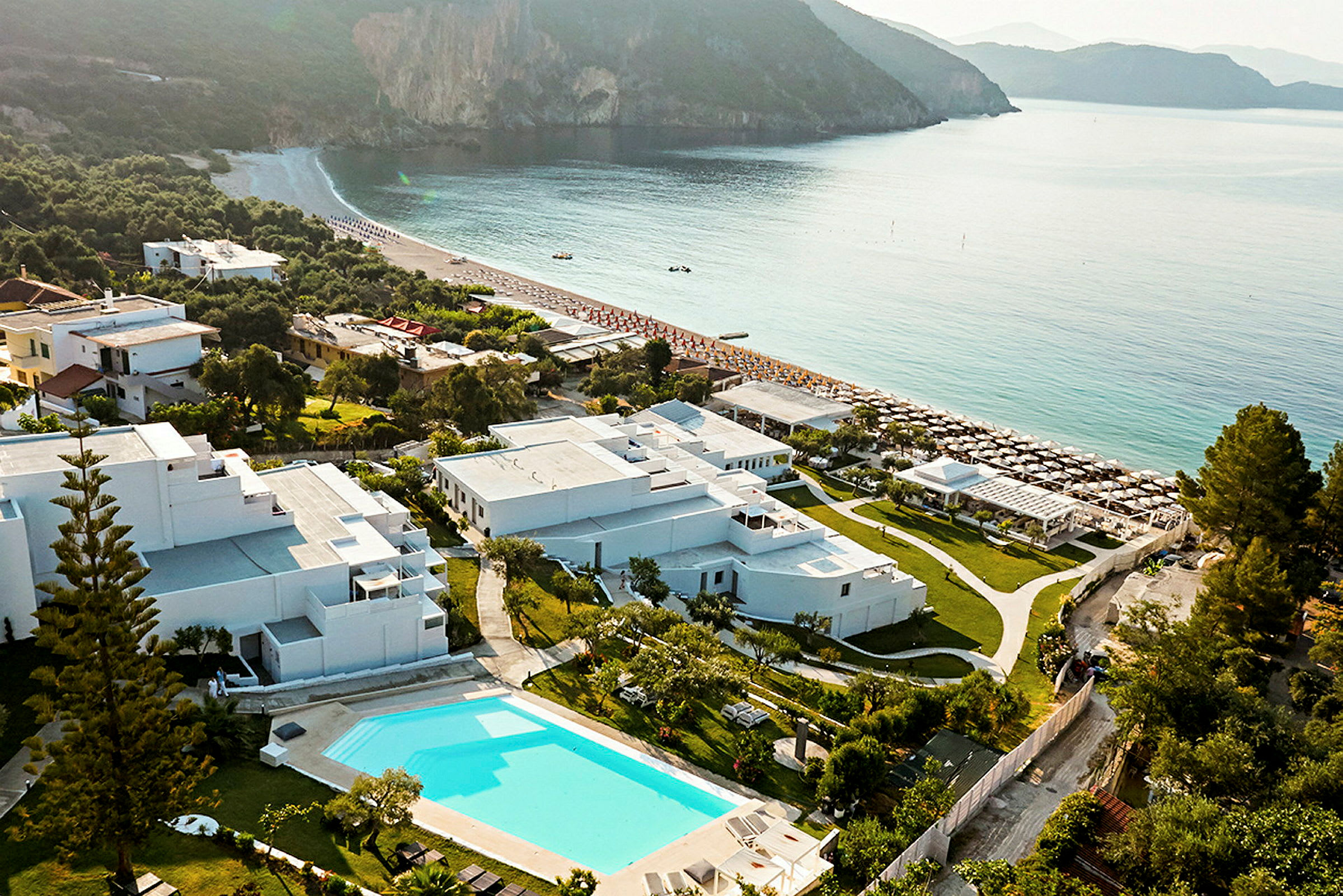 Flygvy av semesteranläggning med pool och omgivande byggnader vid havet. (AI-genererad text)