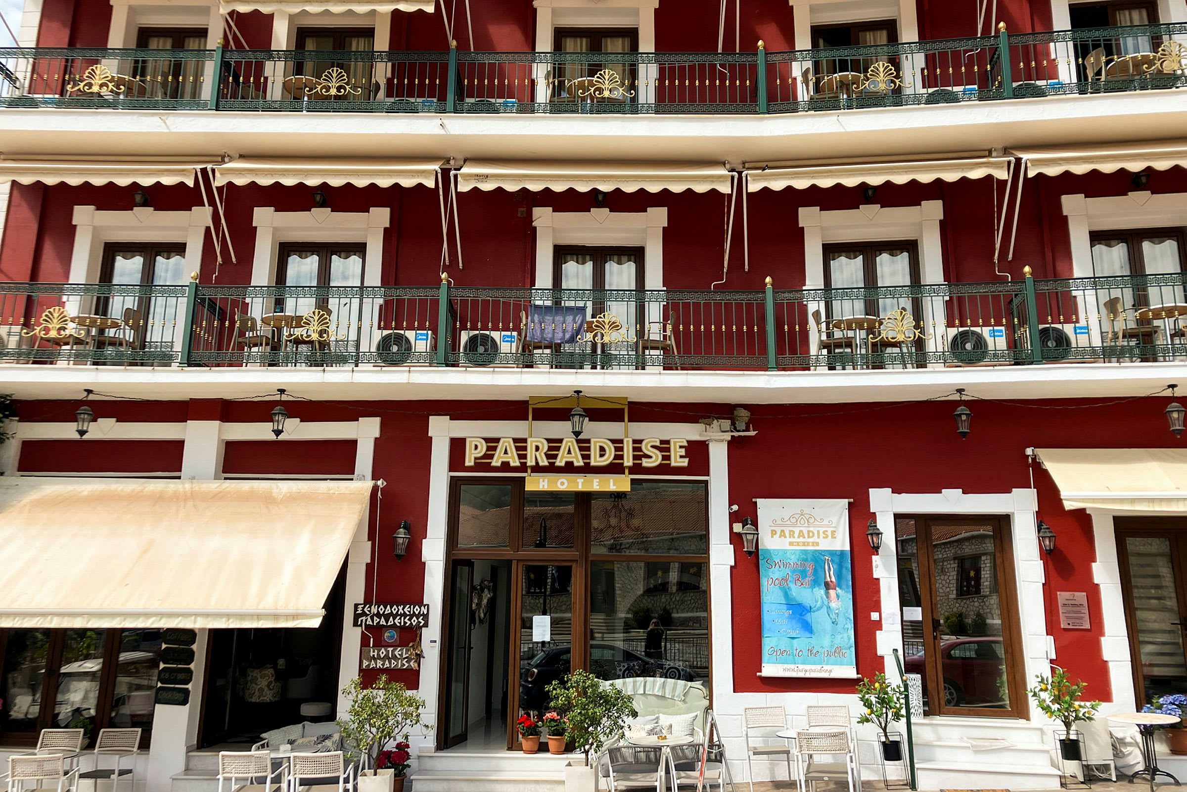 Två våningar av hotellet Paradise i en röd byggnad med balkonger och vit dekoration. (AI-genererad text)