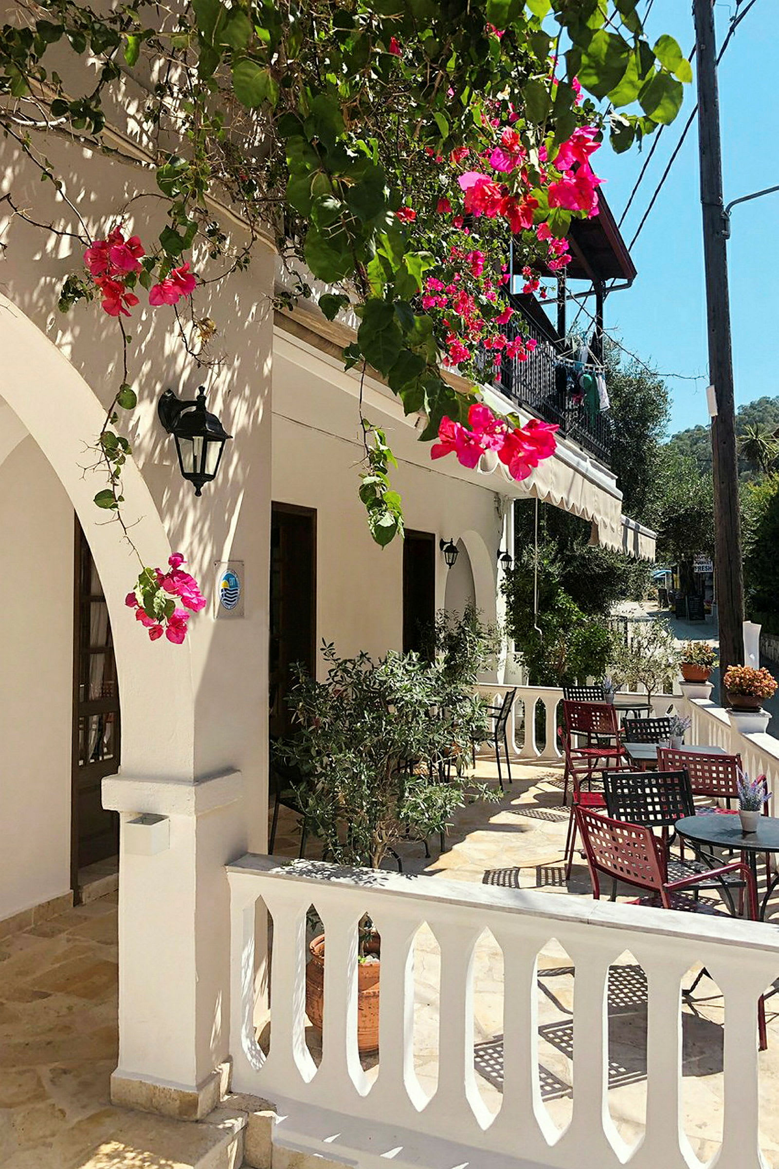 En solig uteplats med vita balustrader och bord omgivna av blommande bougainvillea. (AI-genererad text)