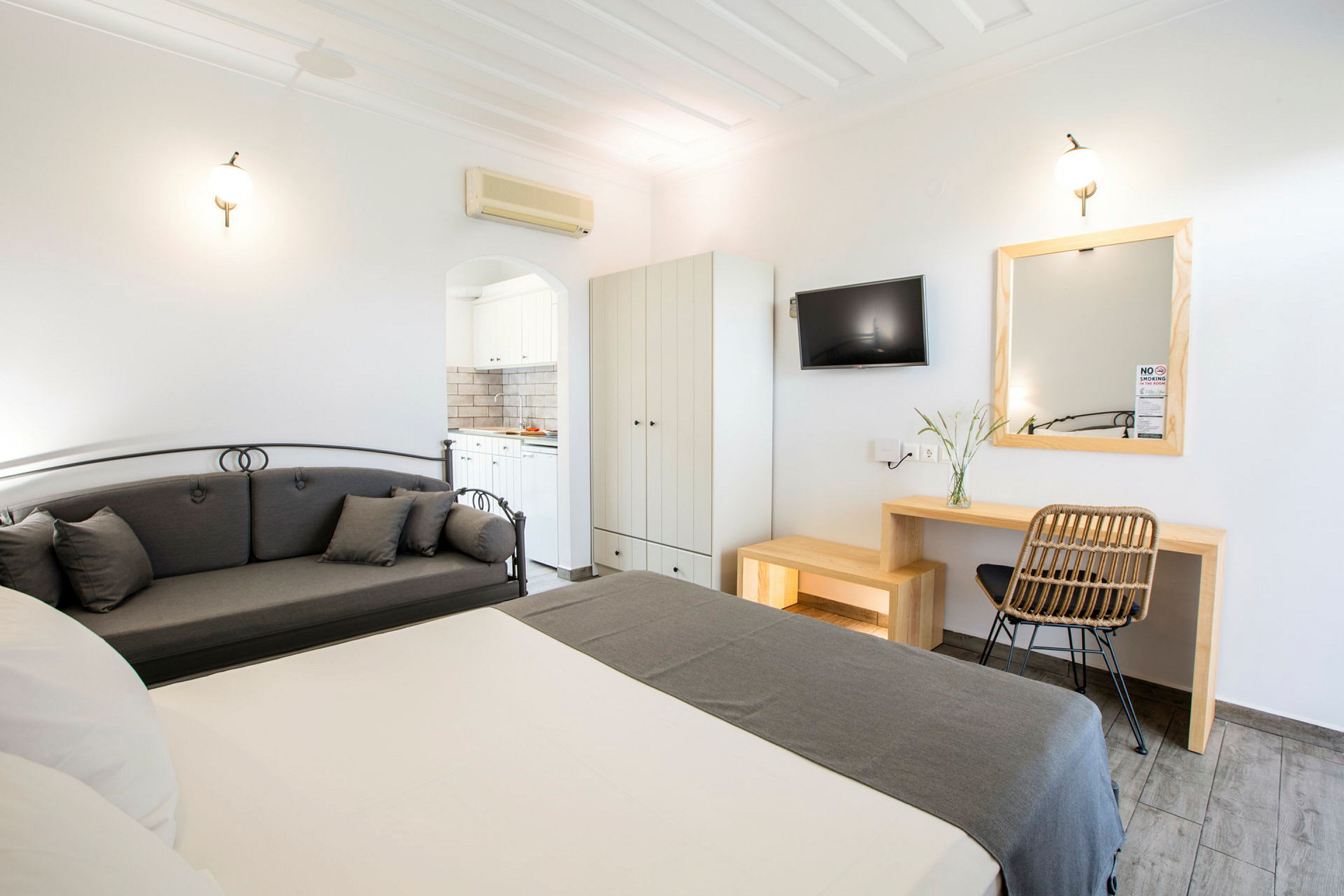 Ett hotellrum med säng, grå soffa, skrivbord, väggmonterad TV och garderob. Ett badrum syns genom en dörröppning. (AI-genererad text)