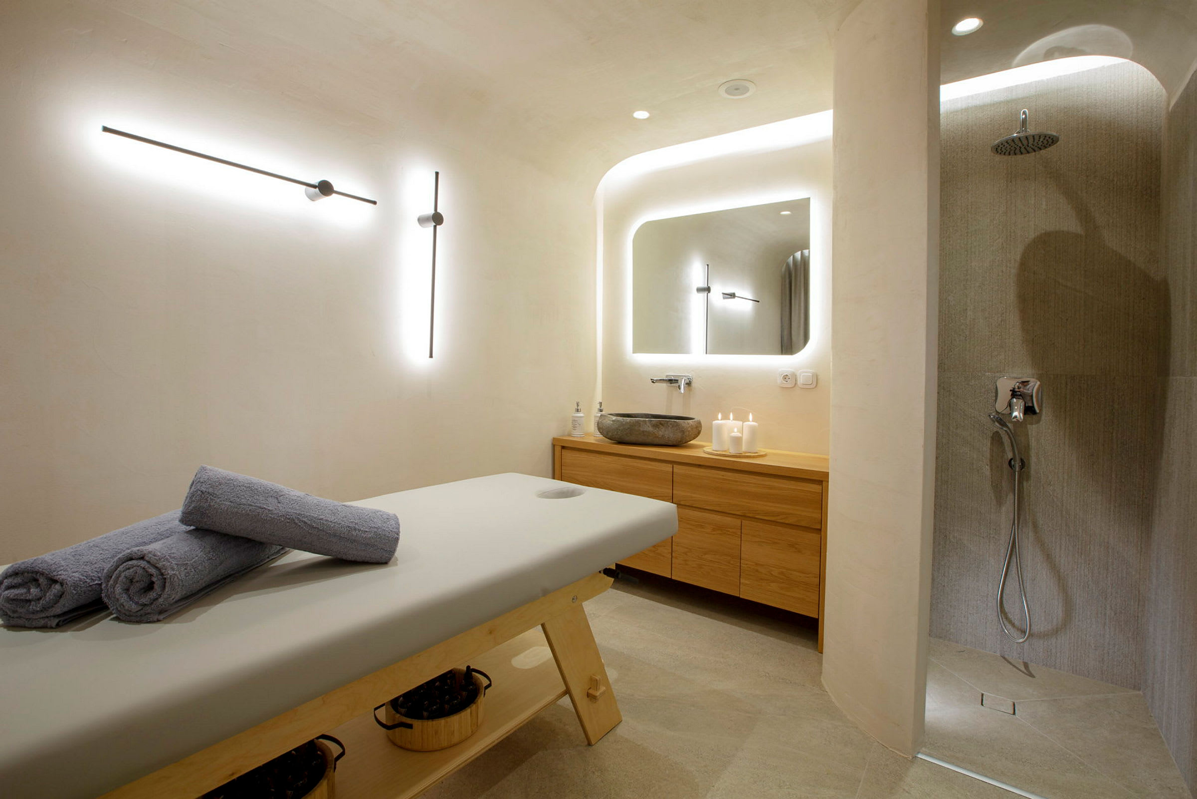 Ett spa-rum med en massagebänk, handdukar, en dusch och ett handfat. (AI-genererad text)