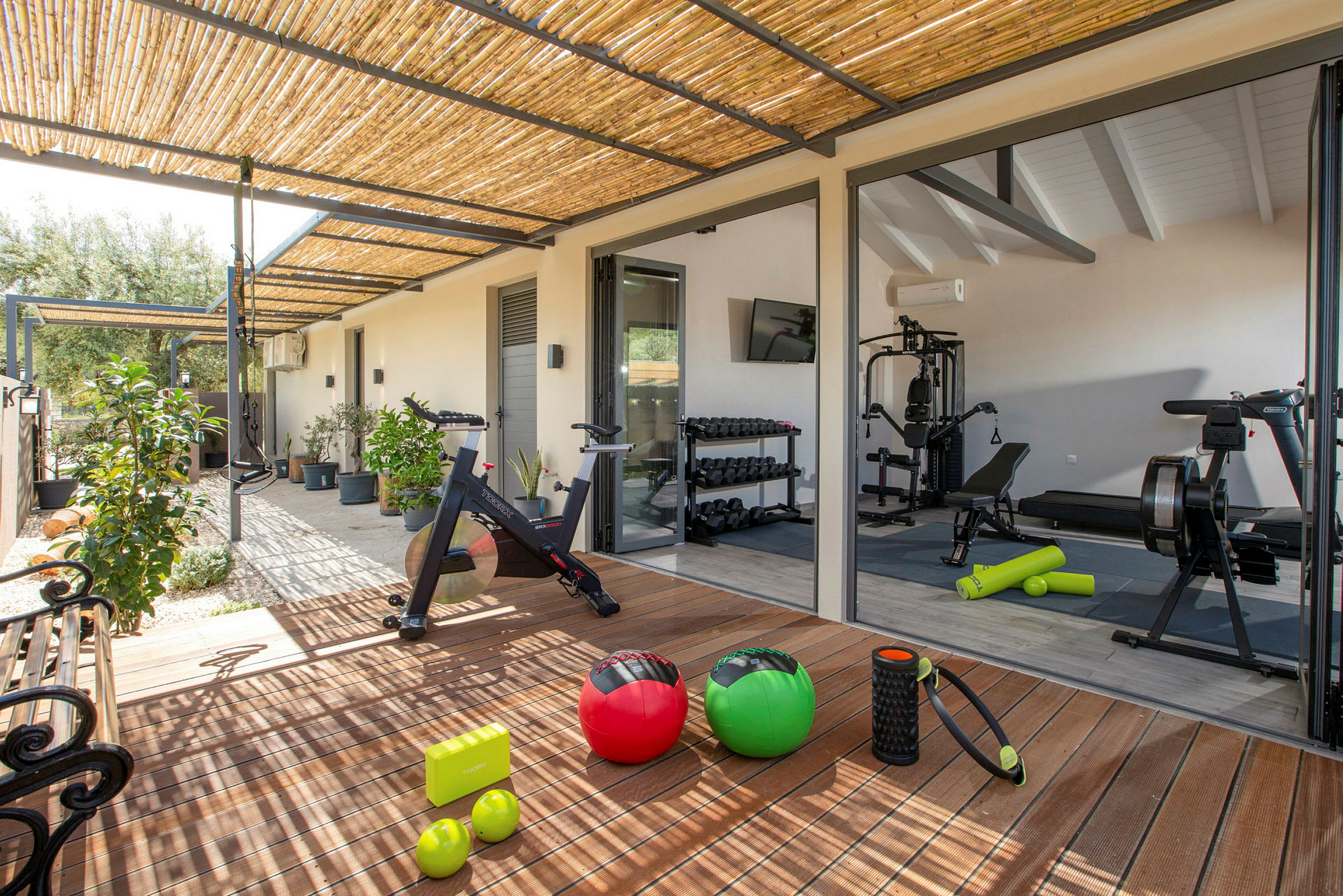 Ett gym med utrustning och träningsredskap vid en uteplats med växter. (AI-genererad text)
