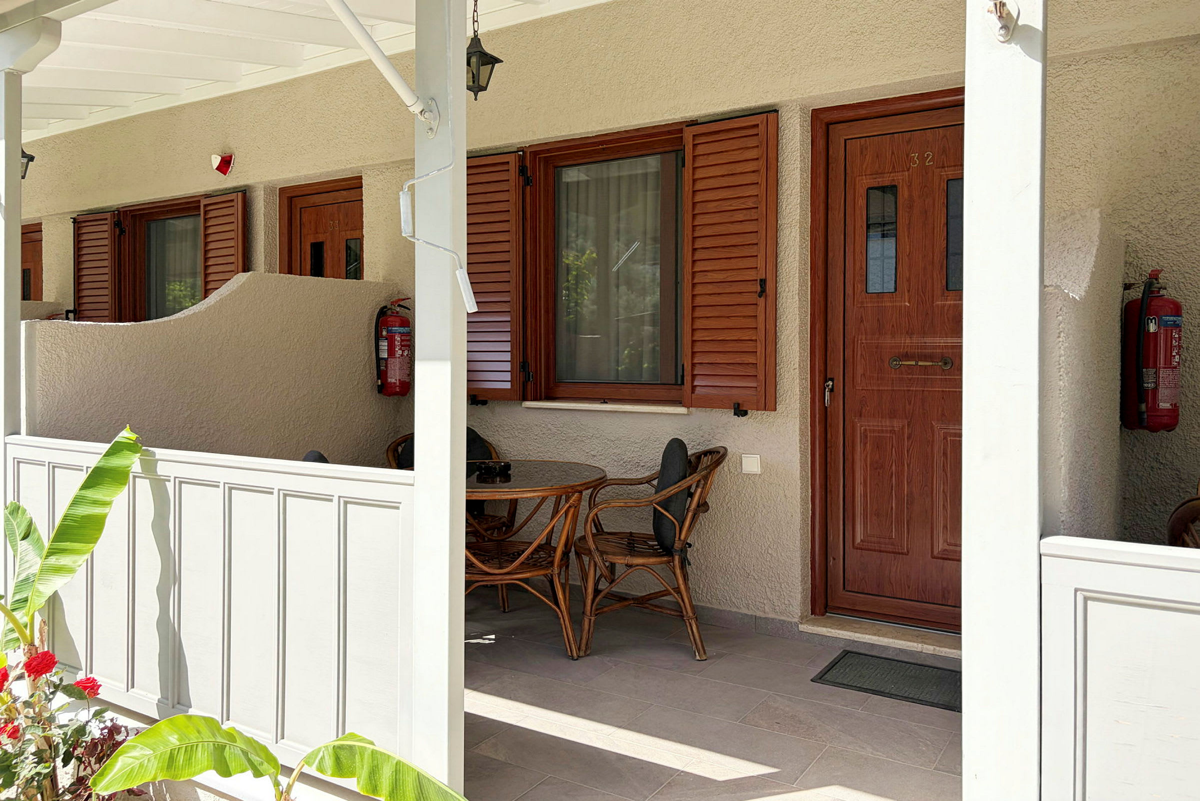 En veranda med ett runt bord och två stolar framför ett hus med trädörr och fönsterluckor. (AI-genererad text)