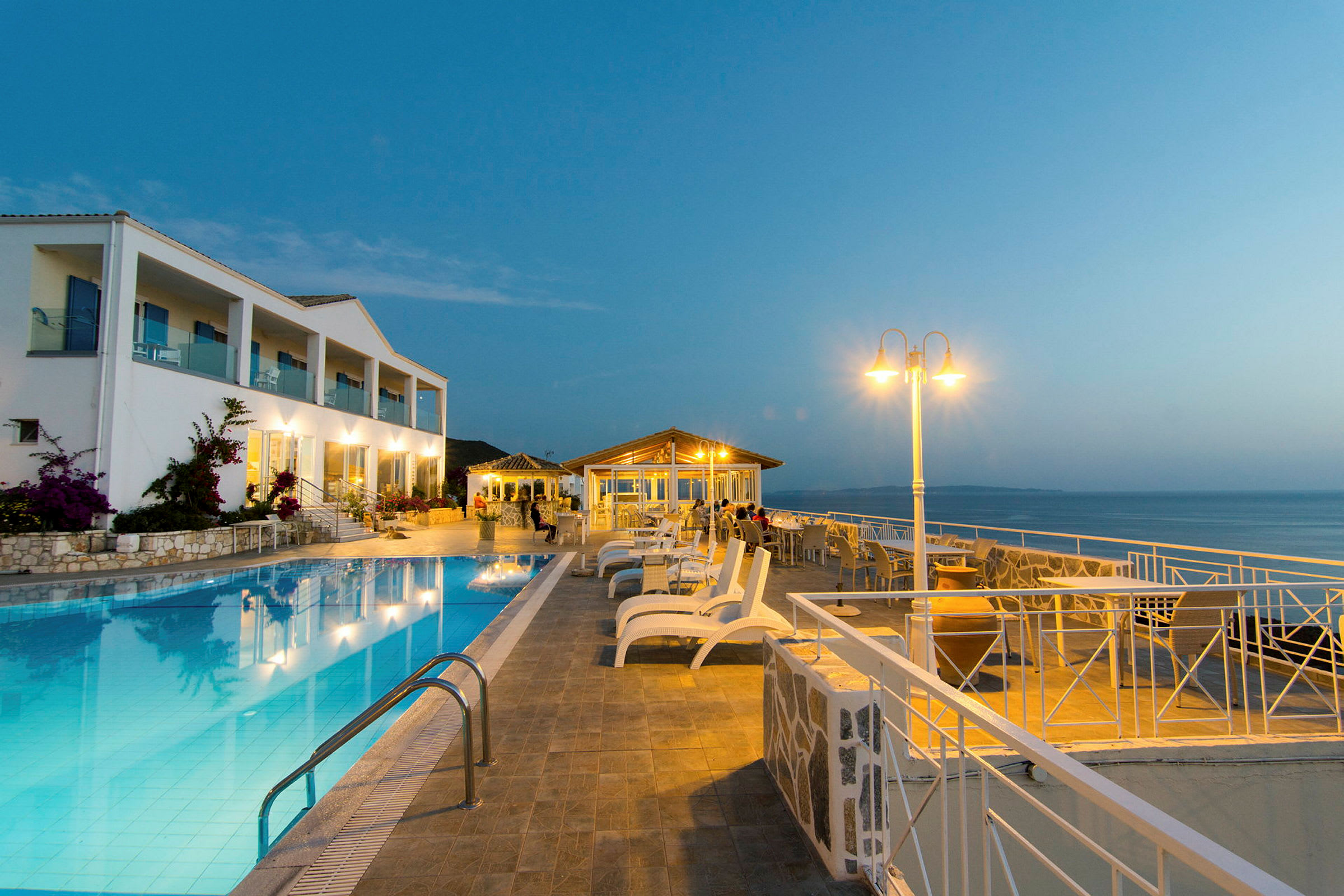 Ett hotellområde på kvällen med en utomhuspool och utsikt över havet. (AI-genererad text)