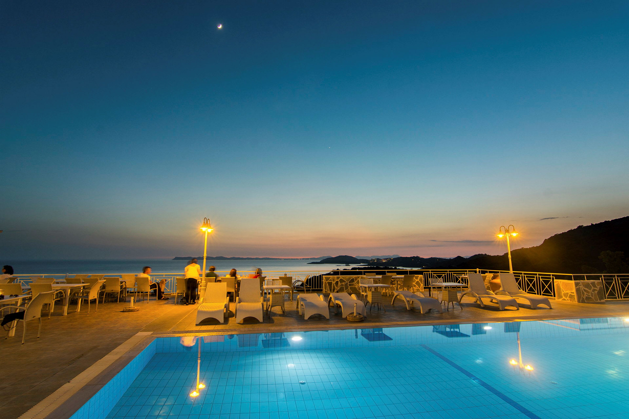 Utsikt över en pool och sittplatser med havet och solnedgången i bakgrunden. (AI-genererad text)