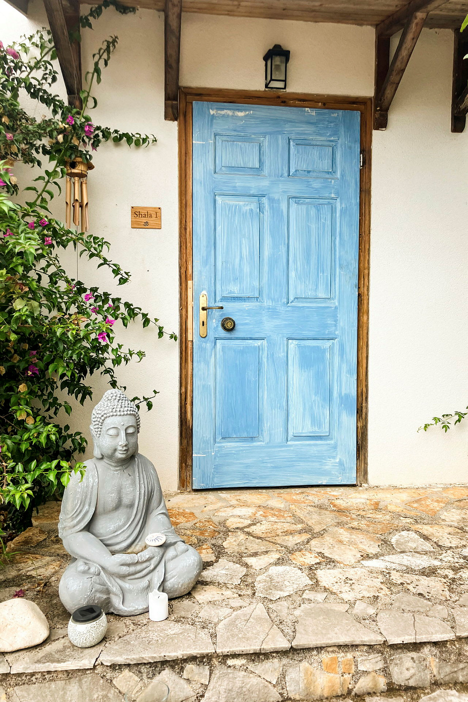 En blå målad dörr med en stenstaty av en sittande Buddha framför. (AI-genererad text)