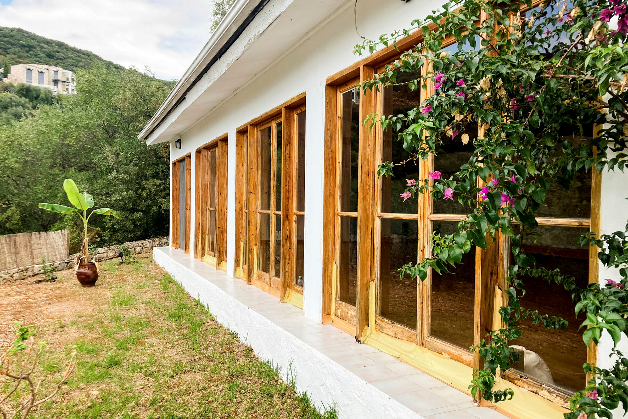 Bild av ett hus med vita väggar och fönster i träramar, omgiven av grönska och blommor. (AI-genererad text)