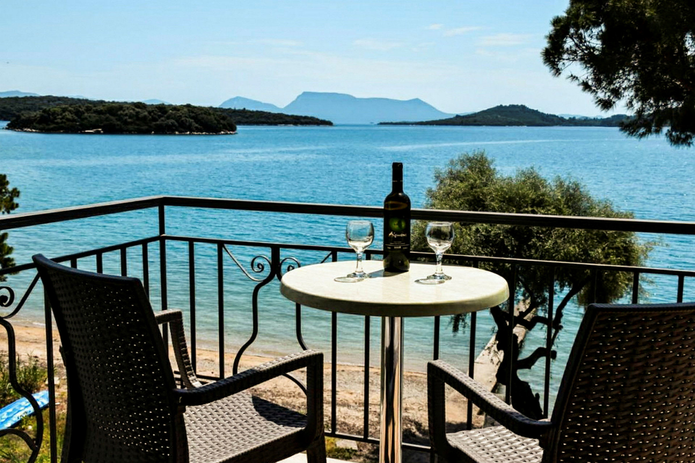Två stolar och ett bord med ett vinflaska och glas på en balkong med utsikt över havet. (AI-genererad text)