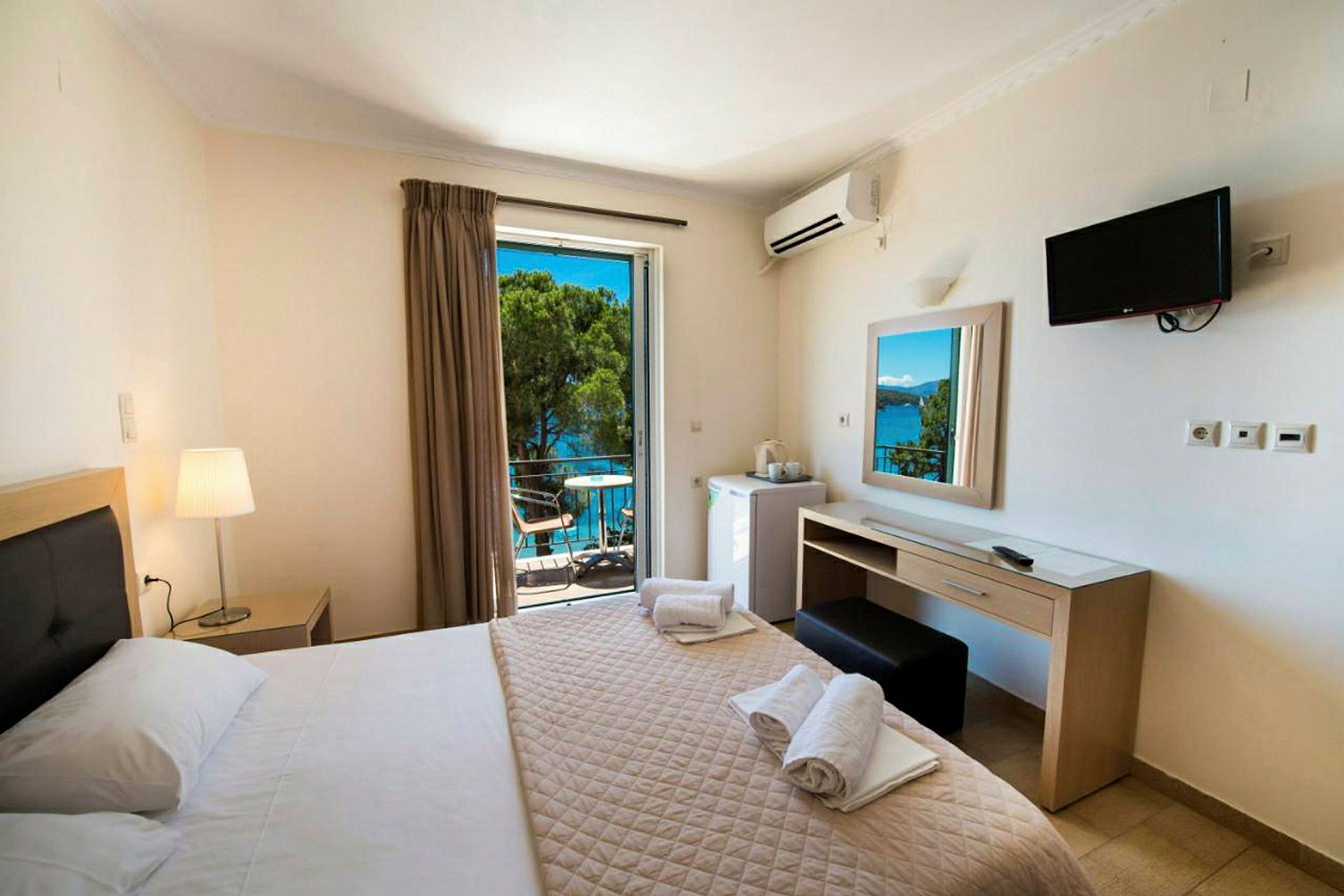 Hotellrum med dubbelsäng, skrivbord, TV och balkong med utsikt över havet. (AI-genererad text)