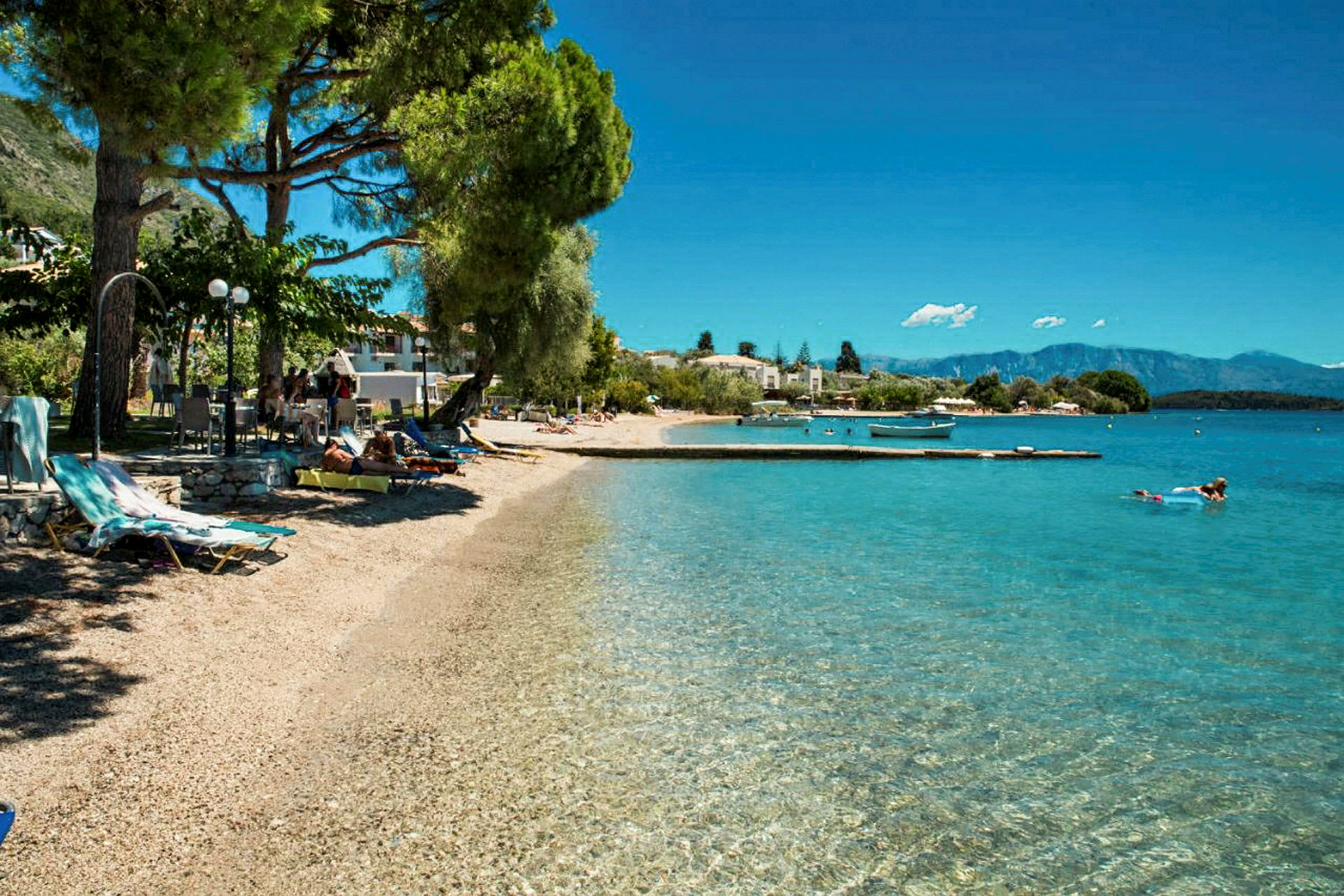 En strand med klart vatten, solstolar och träd. (AI-genererad text)