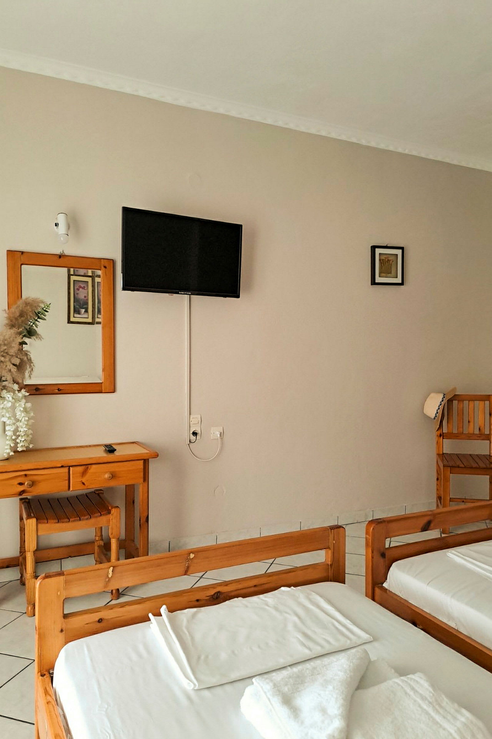 Ett hotellrum med två träsängar, ett skrivbord och spegel, samt en väggmonterad TV. (AI-genererad text)
