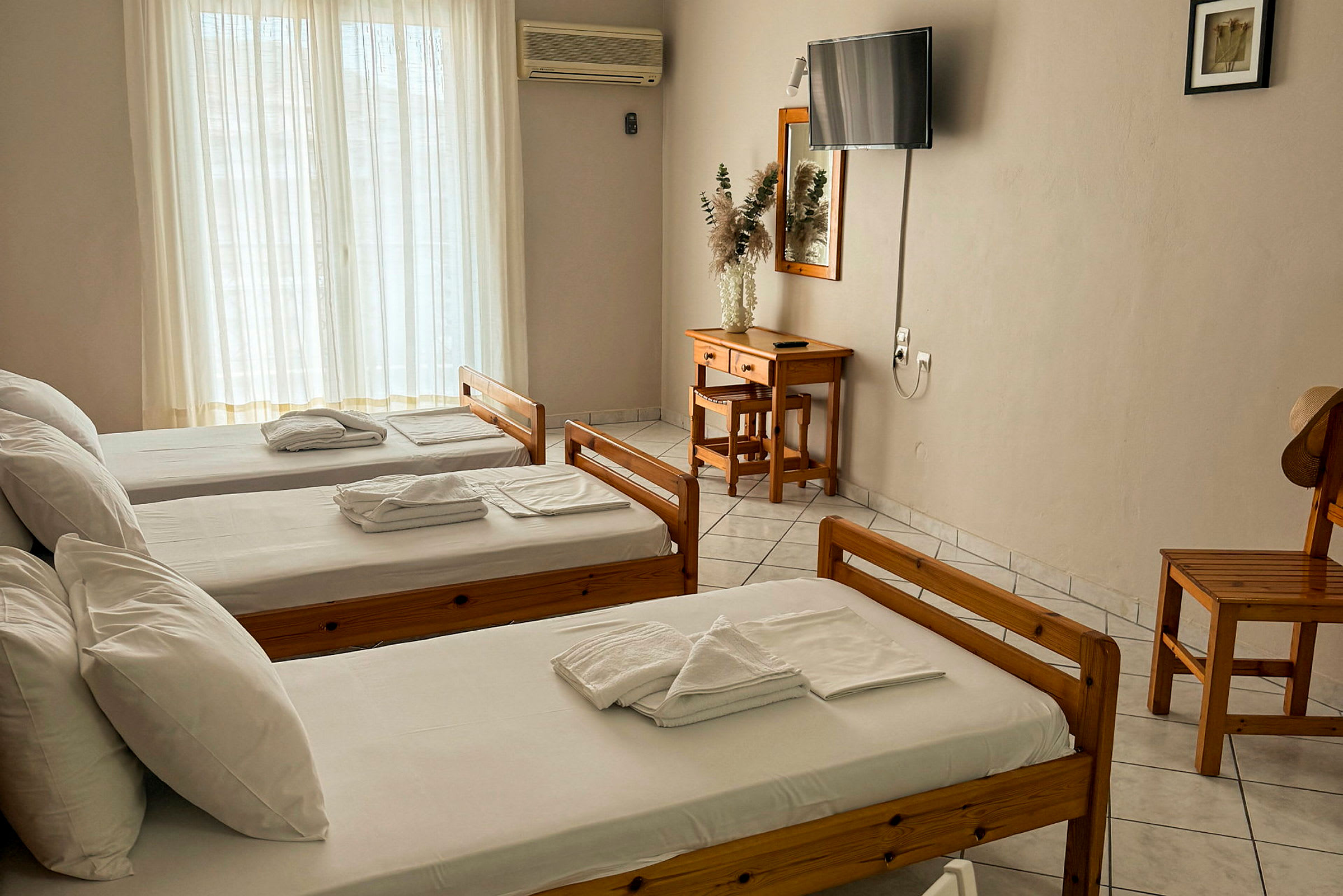 Tre enkelsängar i ett hotellrum med möbler av trä, ett skrivbord och en TV på väggen. (AI-genererad text)
