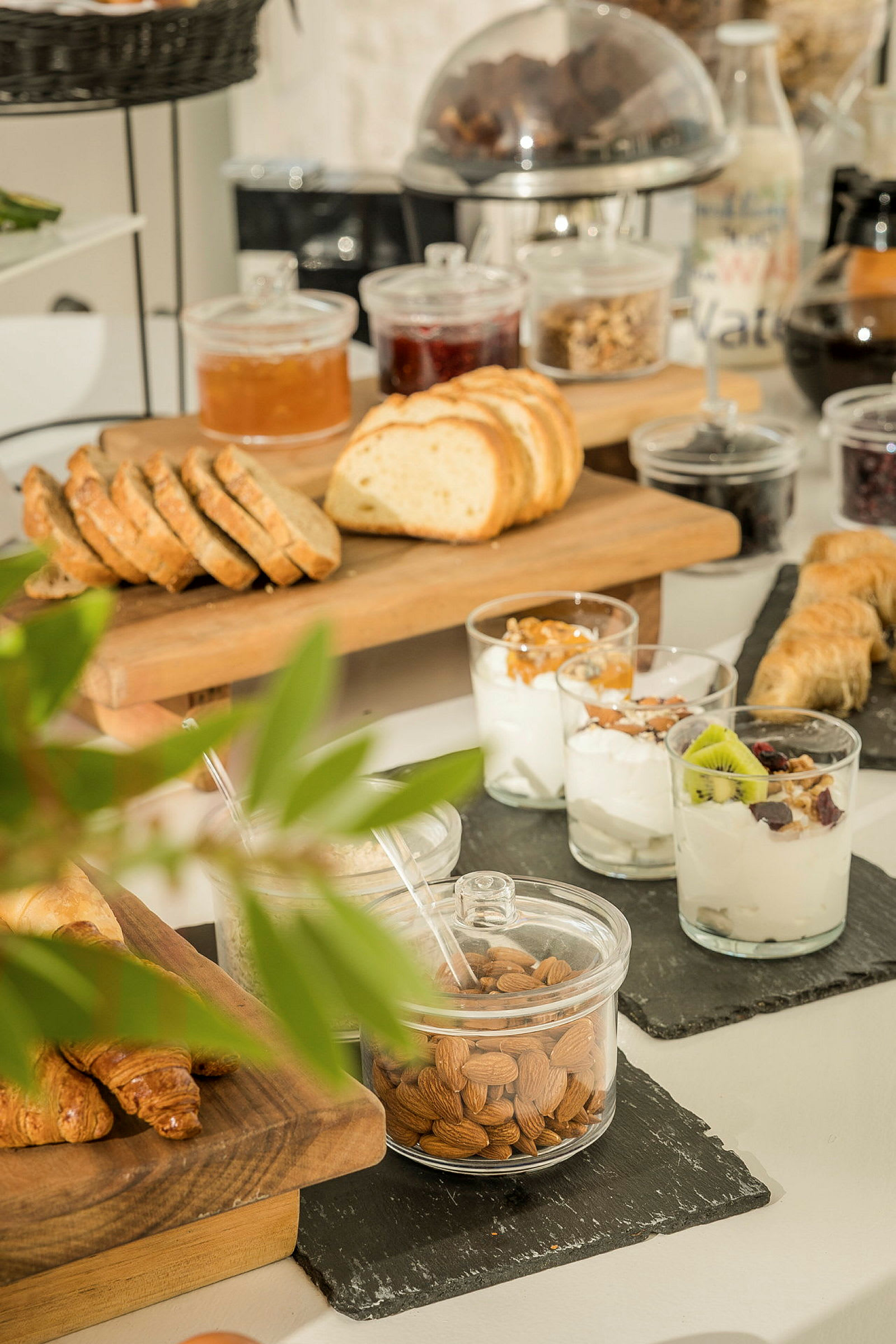 Ett bord med en varierad frukostuppställning inklusive skivat bröd, yoghurt med toppings och croissanter. (AI-genererad text)