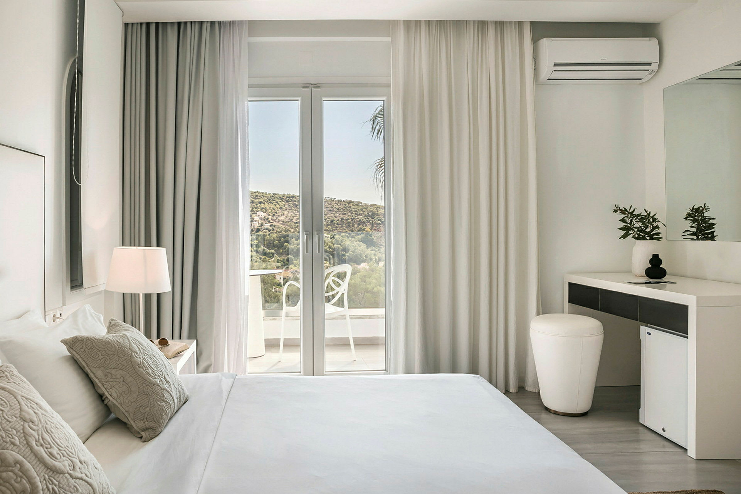 Ett hotellrum med ljus inredning, inklusive en säng, ett skrivbord och en glasdörr som leder till en balkong. (AI-genererad text)