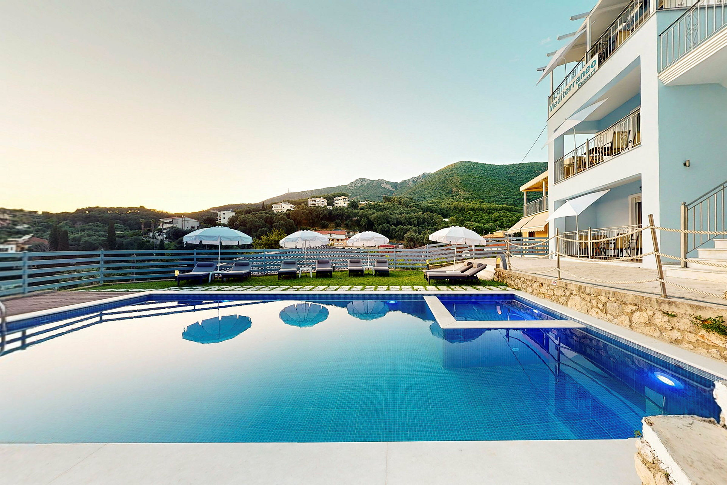 En pool bredvid ett hotell med utsikt över berg och grönska. (AI-genererad text)