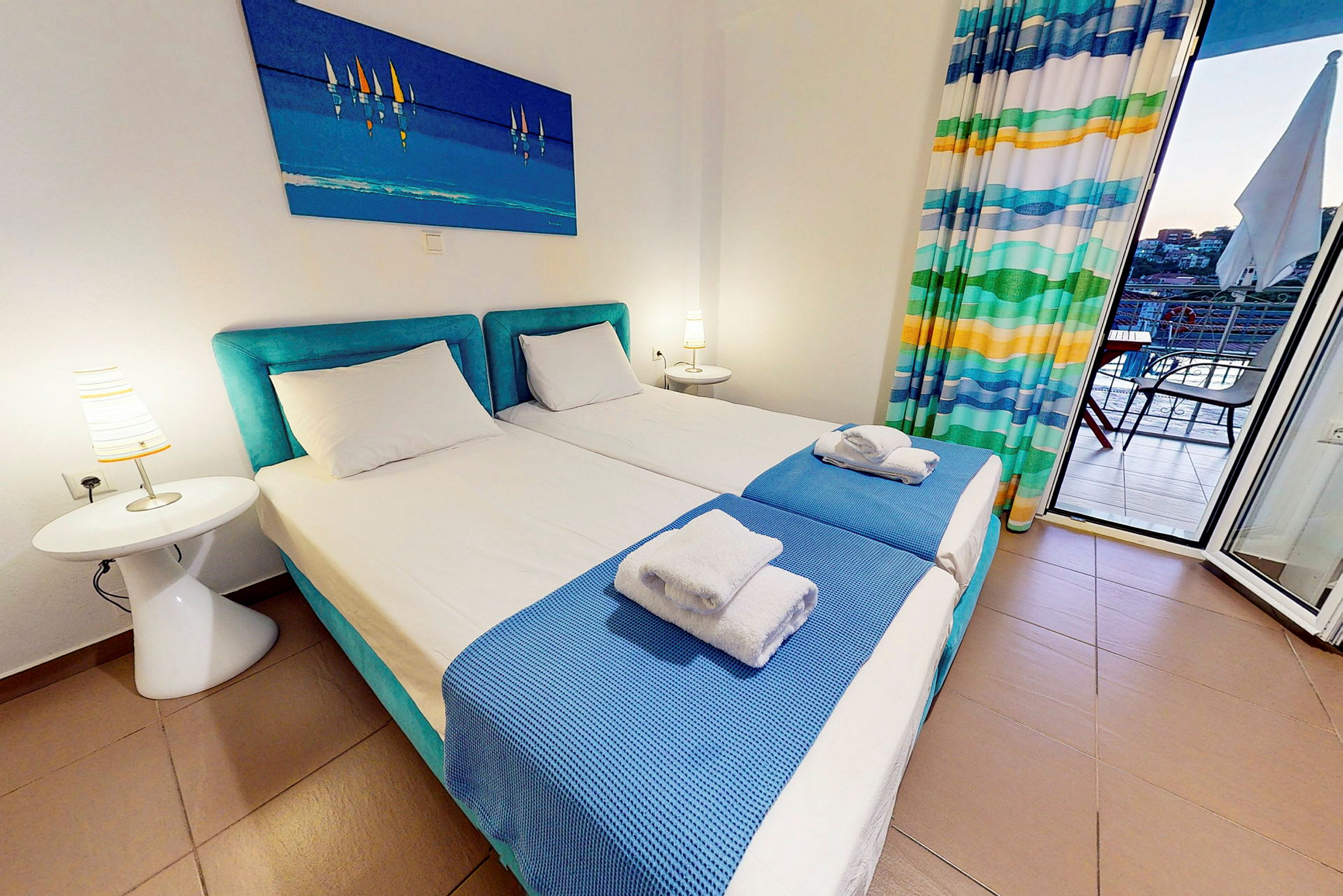 Ett hotellrum med två enkelsängar, blå sängkläder och en tavla ovanför. (AI-genererad text)