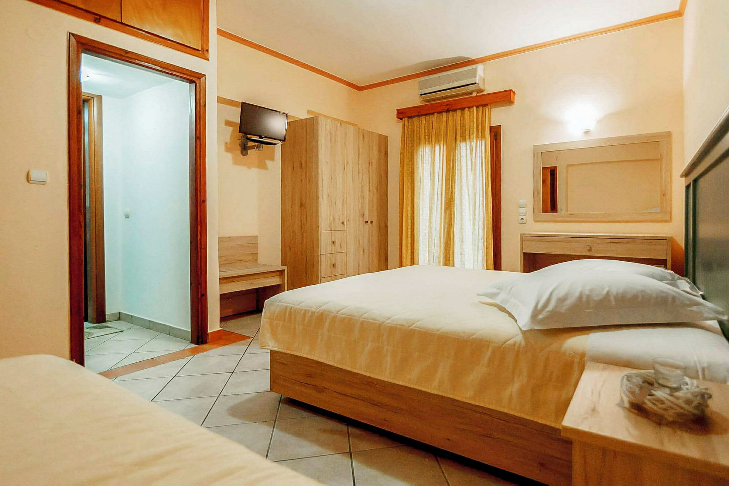 Ett hotellrum med en dubbelsäng, en garderob, en väggmonterad TV och ett fönster med gardiner. (AI-genererad text)