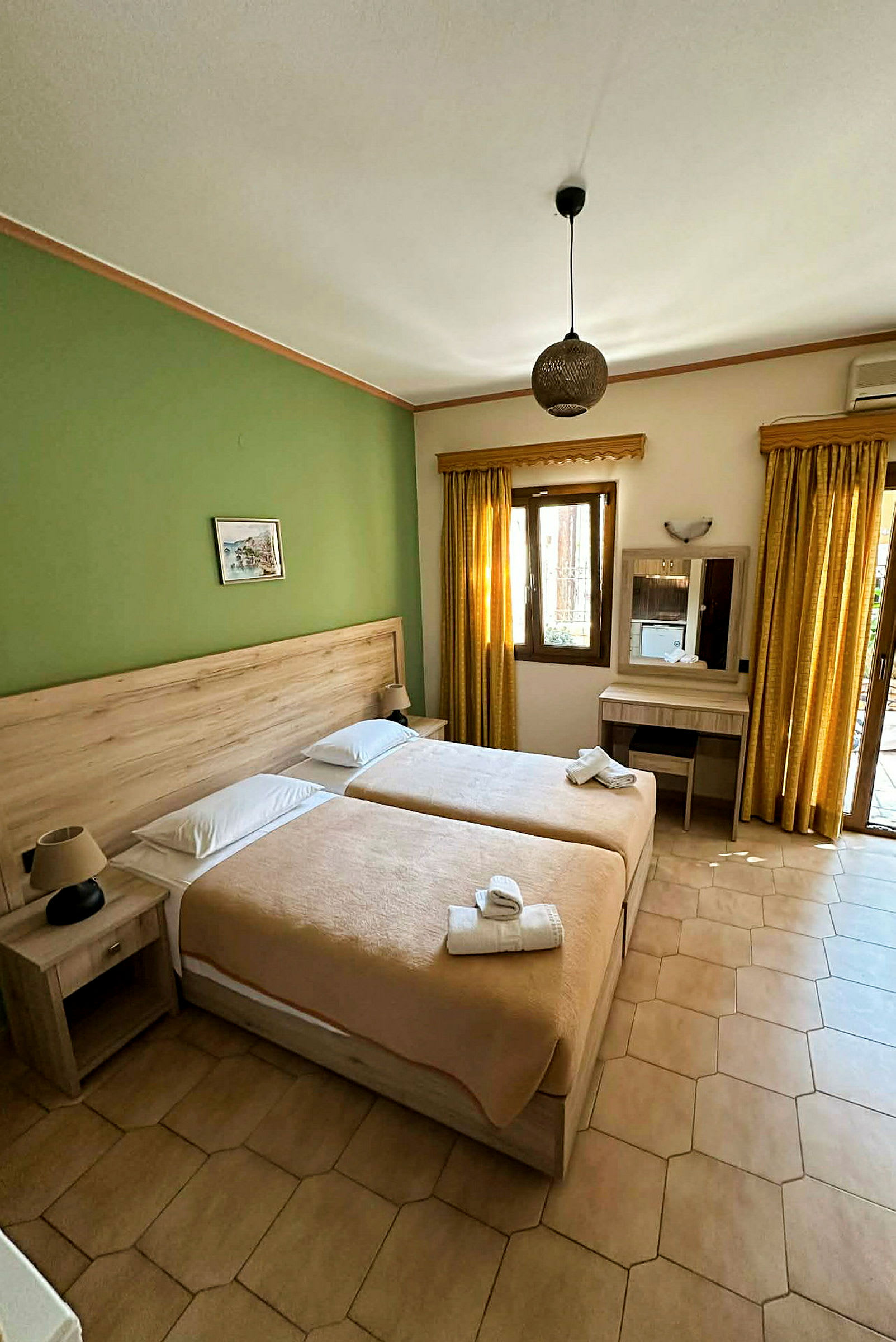 Hotellrum med två enkelsängar, grön vägg, beige sängkläder och möbler, samt fönster med gula gardiner. (AI-genererad text)