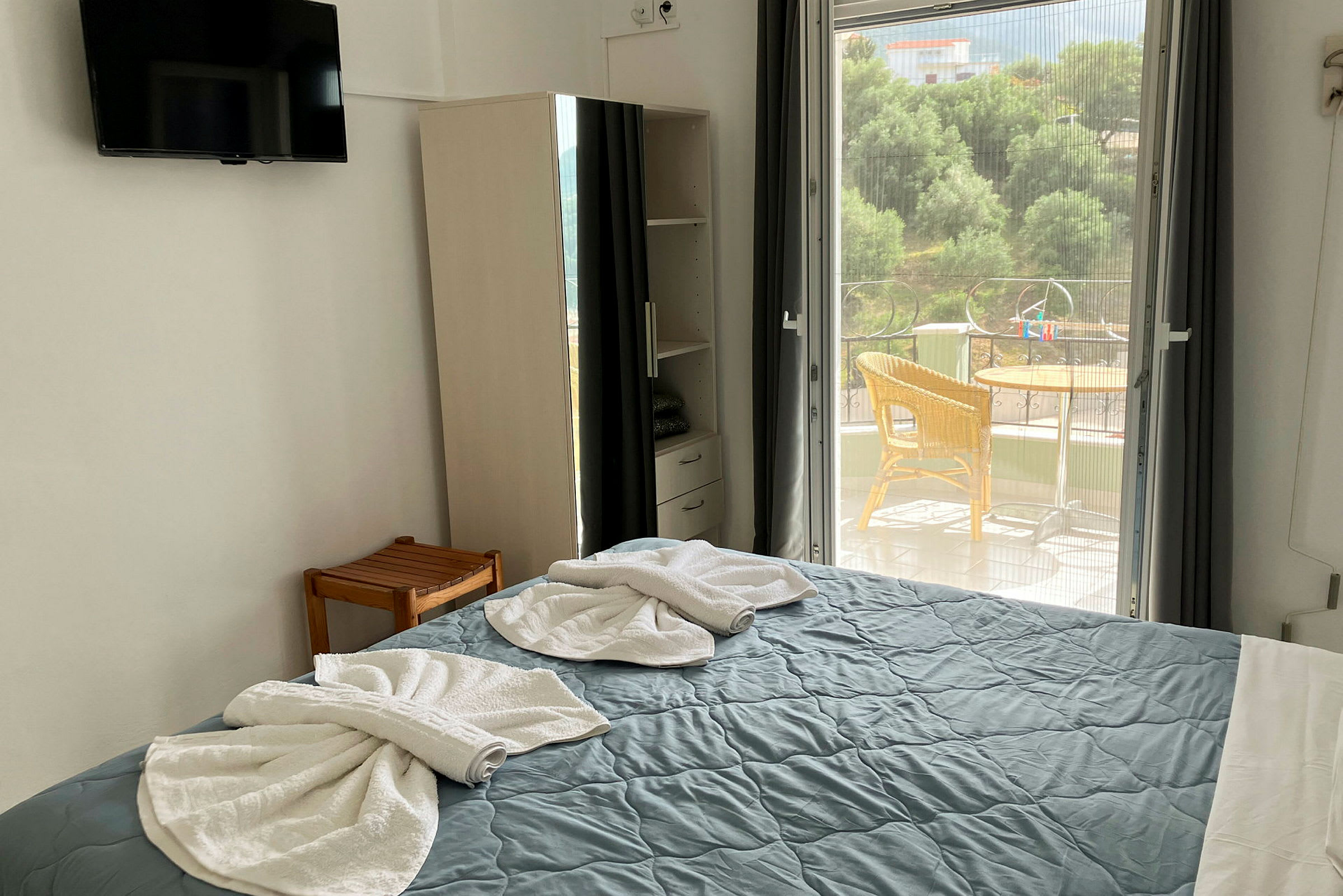 Ett hotellrum visar en bäddad säng med vikta handdukar, en garderob och en utgång till en balkong. (AI-genererad text)