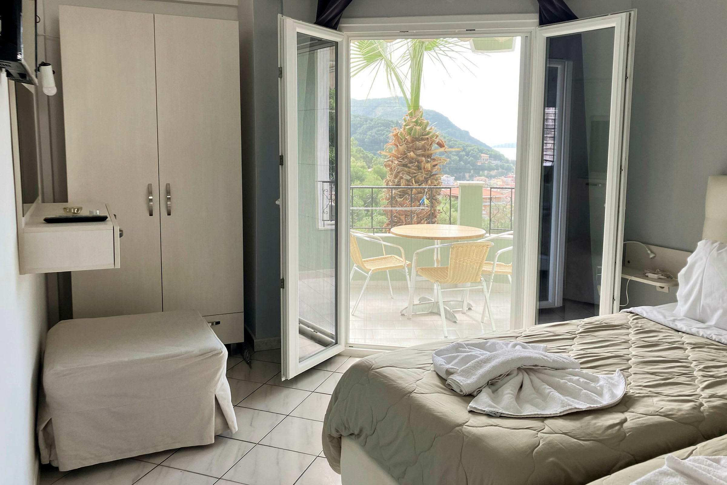 Hotellrum med utsikt mot en terrass med bord, stolar och en palm. (AI-genererad text)