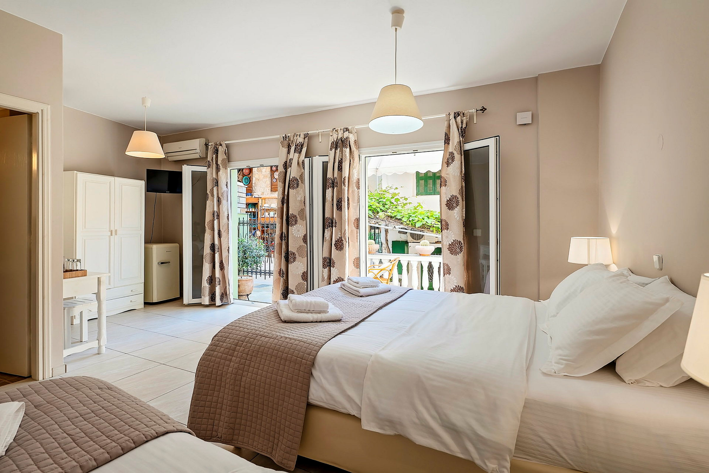 Ett välbelyst hotellrum med två sängar och öppna glasdörrar som leder till en liten terrass. (AI-genererad text)