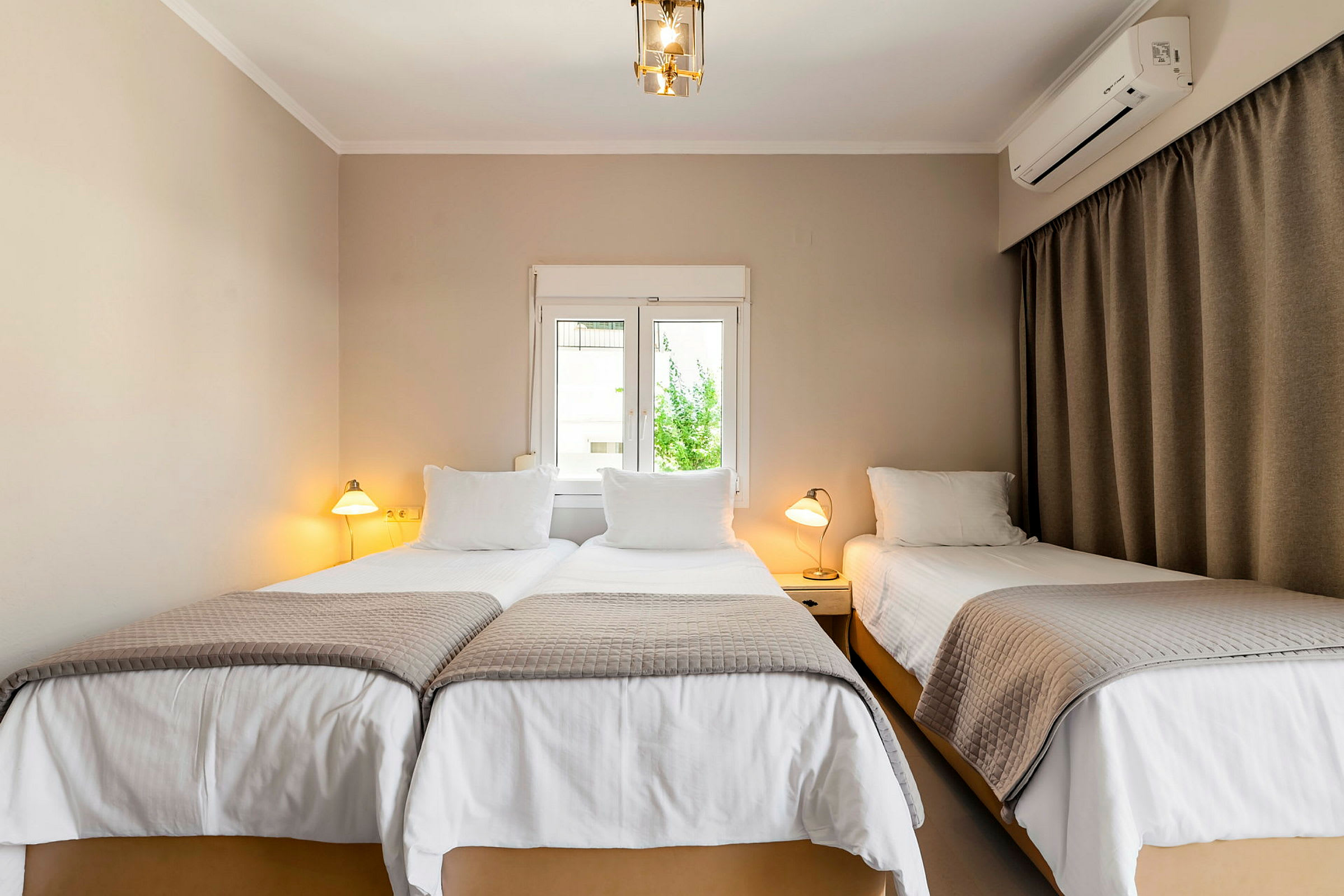 En hotellrum med tre enkelsängar, två ihop och en separat, alla med vita lakan och gråa överkast. (AI-genererad text)