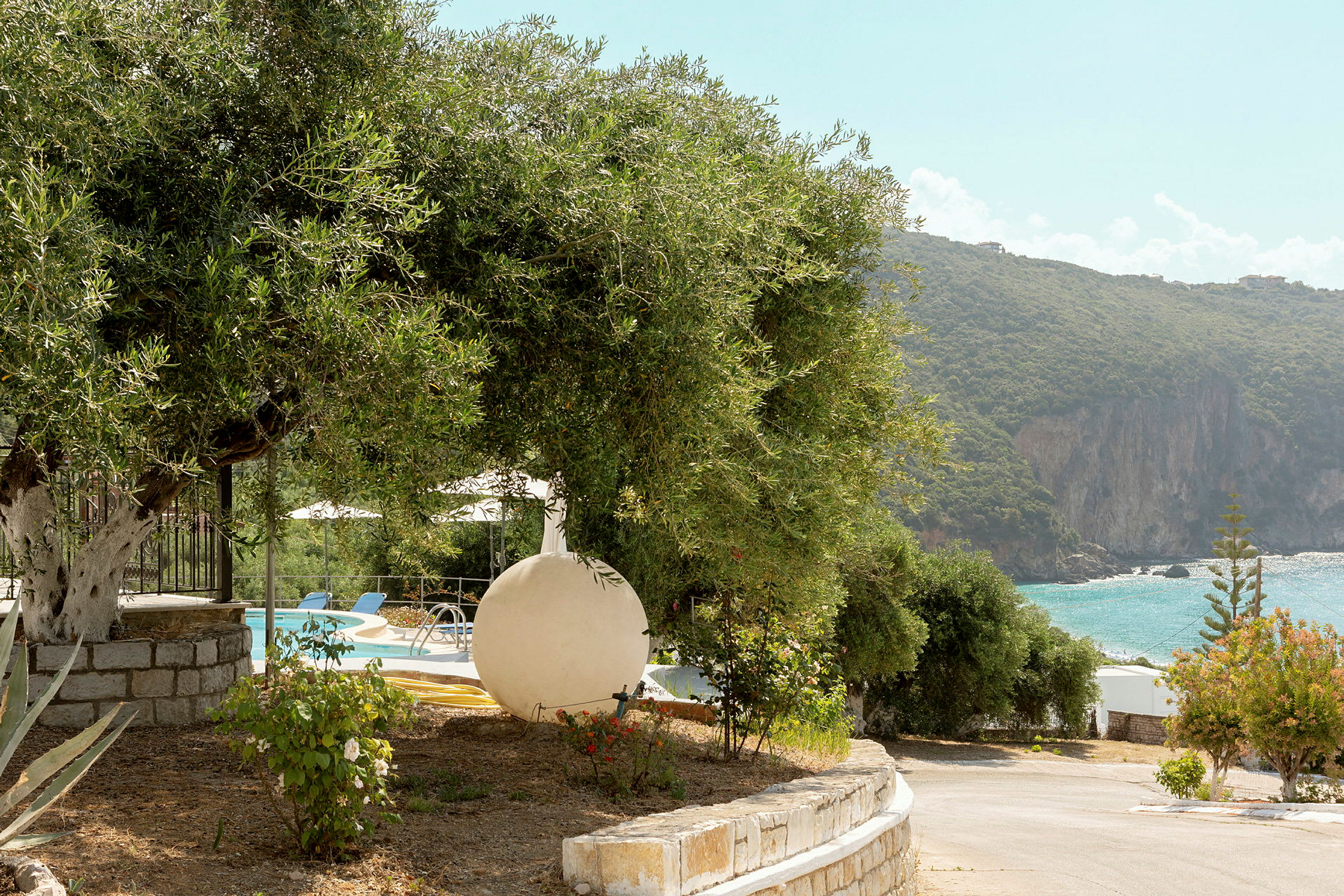 Utsikt över en pool med omgivande vegetation och en strand med klippor vid havet. (AI-genererad text)