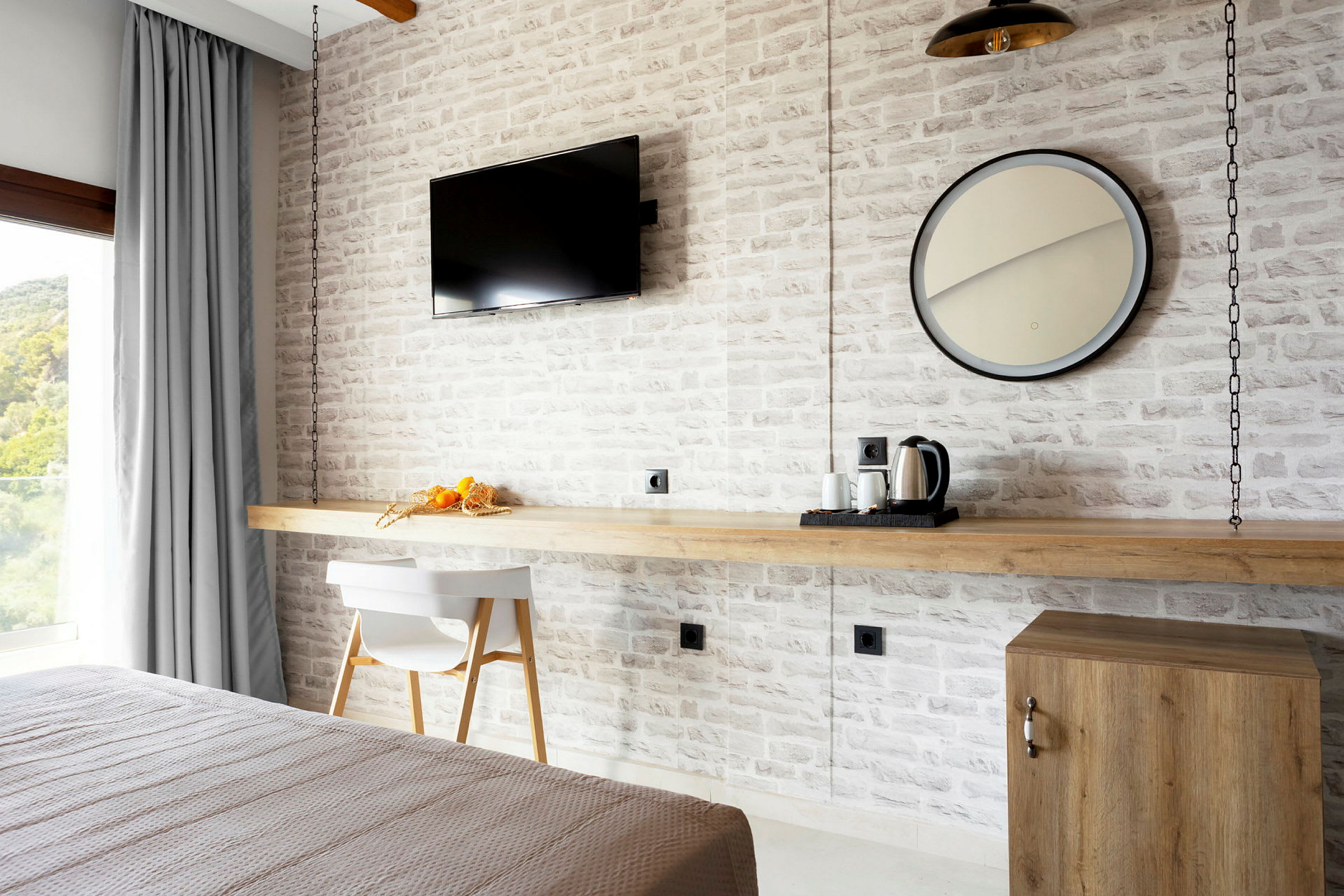 Ett hotellrum med en vit tegelvägg, en modern TV, ett runt spegel, och bord med kaffebryggare. (AI-genererad text)