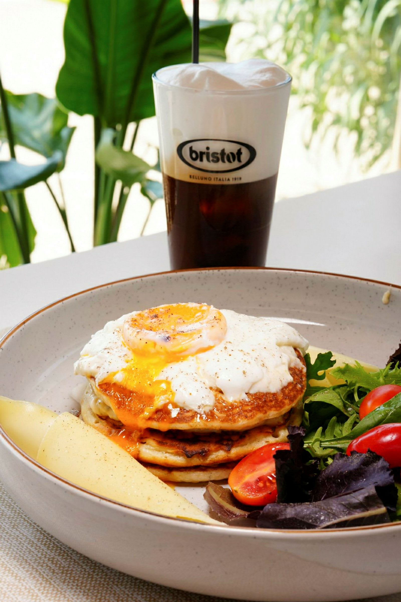 En tallrik med pannkakor, stekt ägg på toppen, sallad och en drink i bakgrunden. (AI-genererad text)