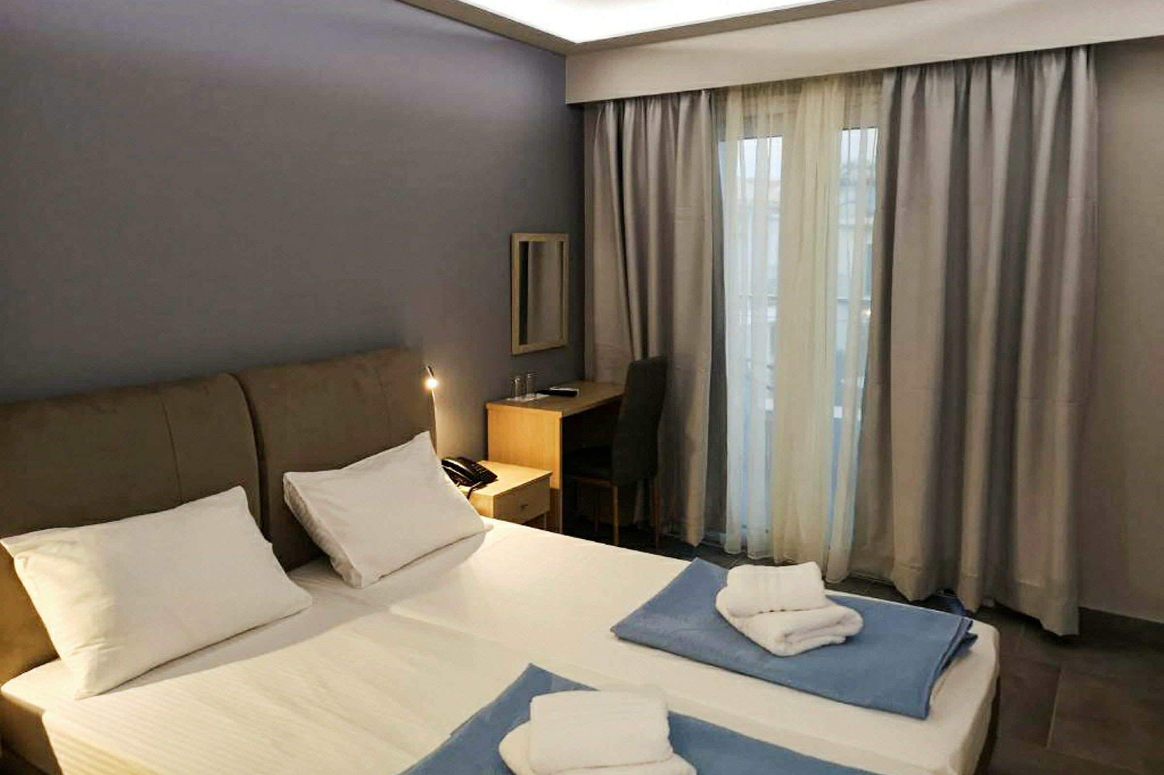 Ett hotellrum med en dubbelsäng, skrivbord och ett fönster med gardiner. (AI-genererad text)