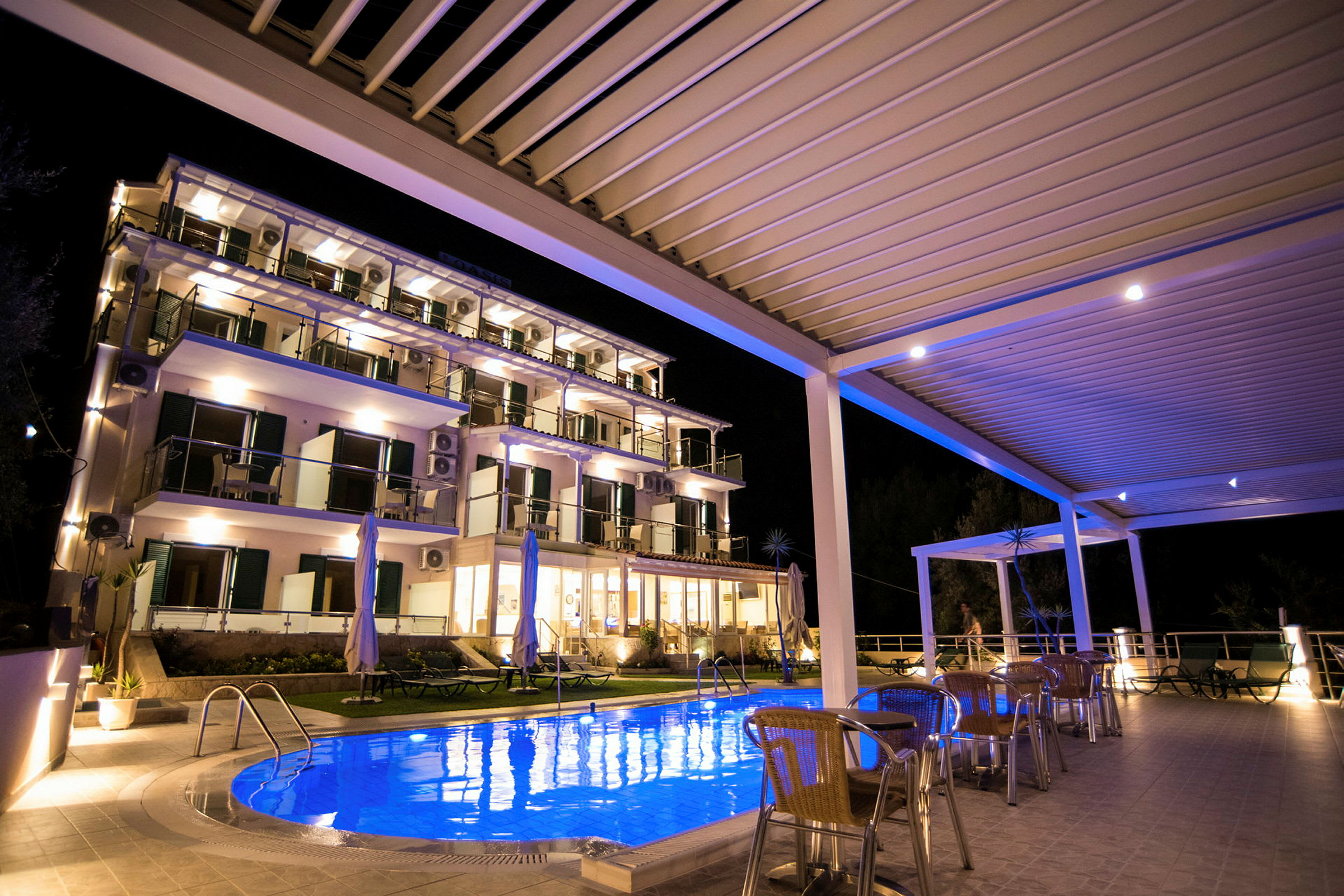 Ett hotell med belyst pool och utemöbler på kvällstid. (AI-genererad text)