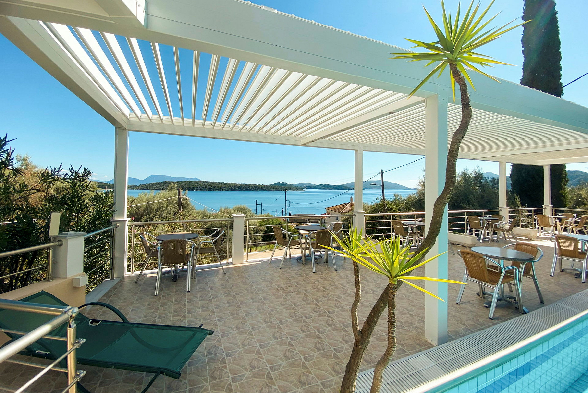 Terrass med sittplatser under en vit pergola, utsikt över havet och omgivande vegetation. (AI-genererad text)