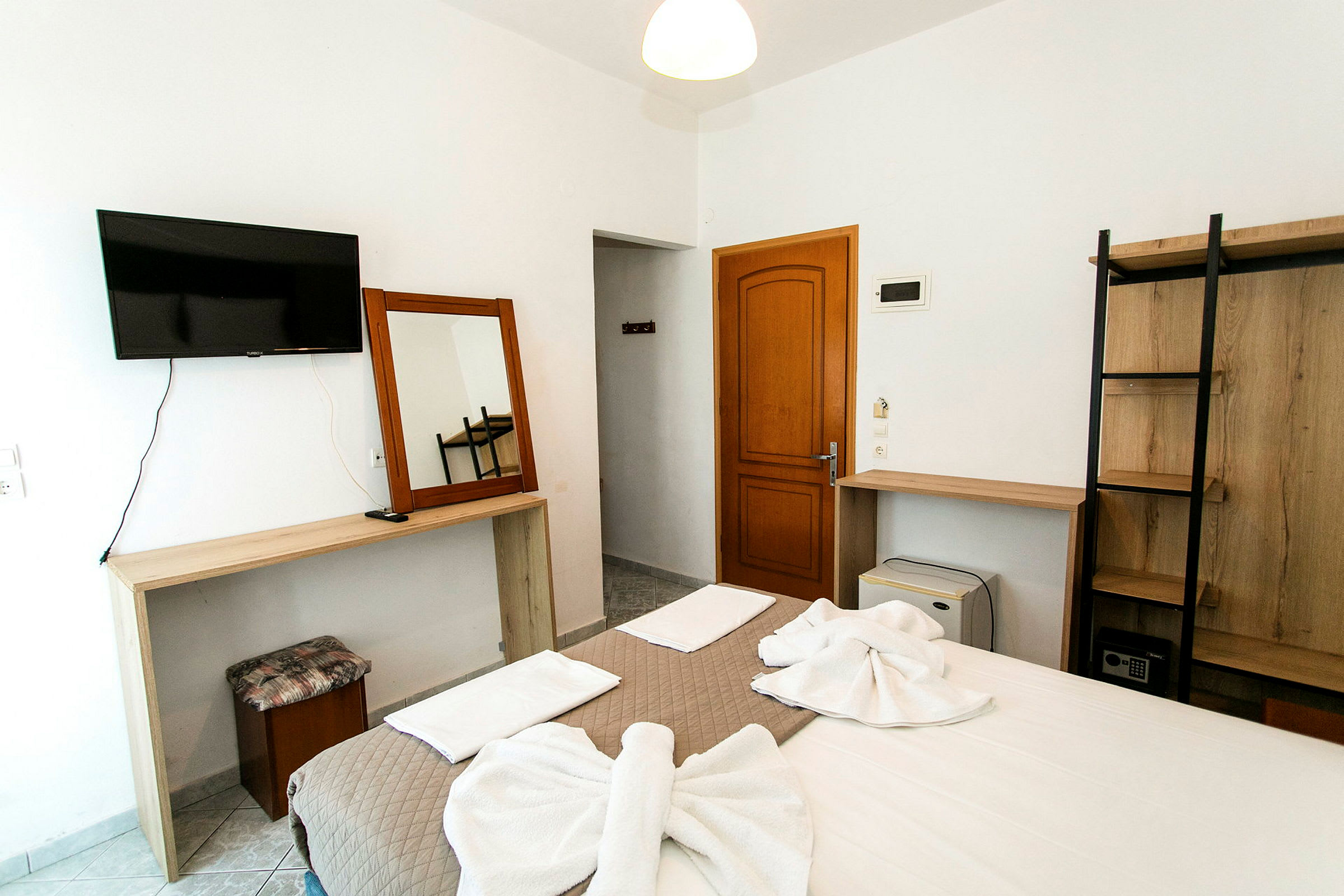 Ett hotellrum med en dubbelsäng som har vikta handdukar på sig, en TV på väggen, ett träskrivbord och en garderob. (AI-genererad text)