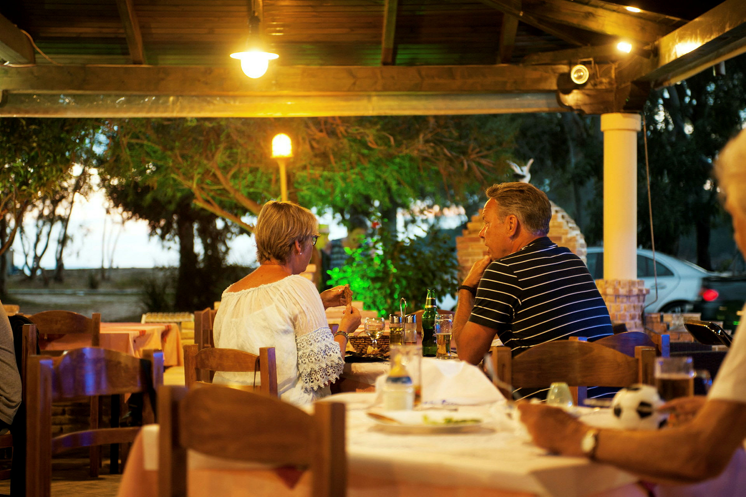 Personer sitter vid ett bord på en utomhusrestaurang omgiven av grönska. (AI-genererad text)