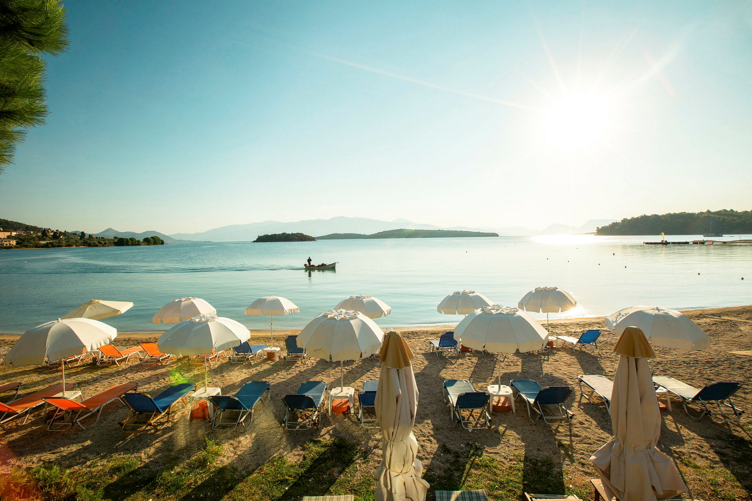 Strand med solstolar och parasoll, med havet och små öar i bakgrunden under en klar himmel. (AI-genererad text)
