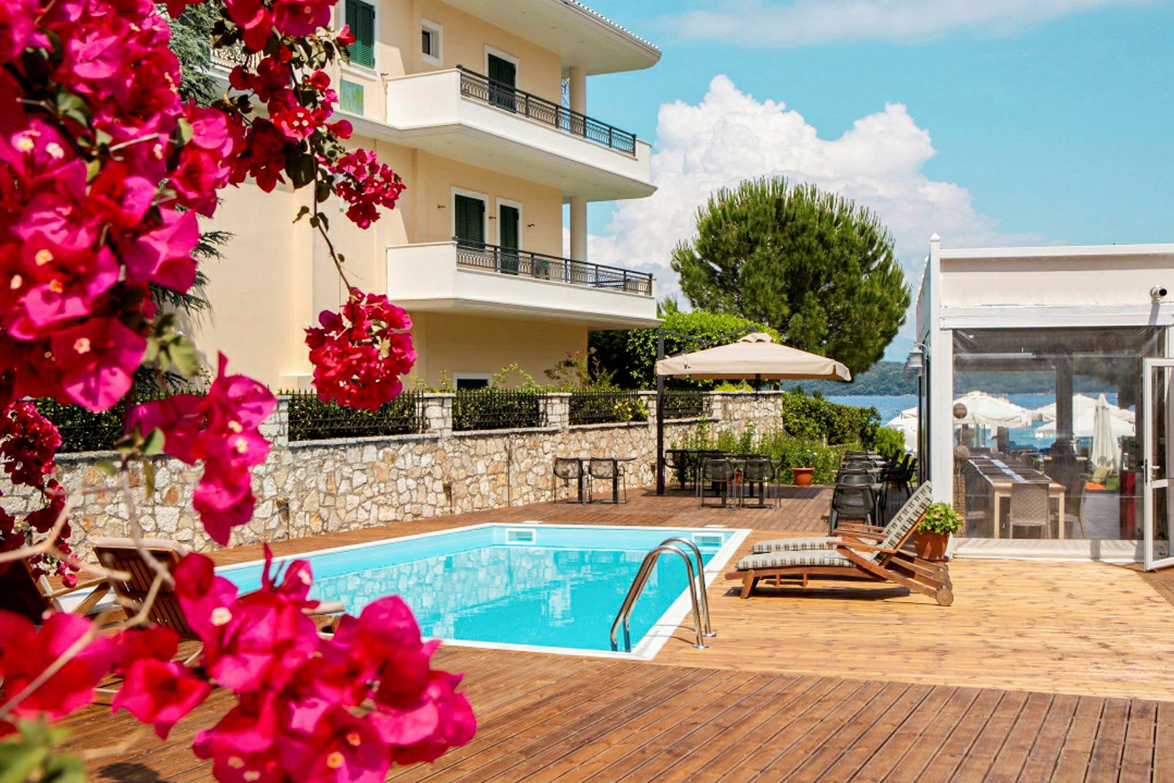 Bild av en byggnad med balkonger, en pool och möbler på en solterrass med blommor i förgrunden. (AI-genererad text)