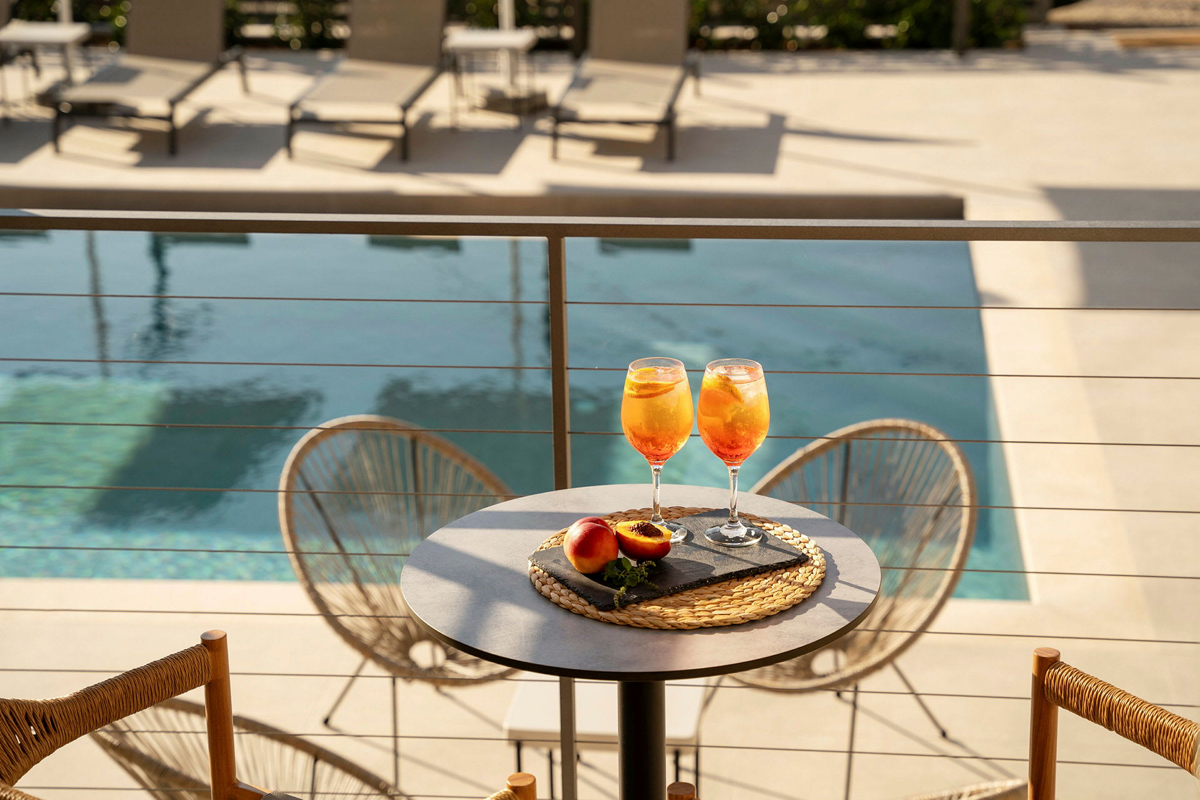 Två glas med apelsindryck och persikor är placerade på ett bord nära en pool. (AI-genererad text)
