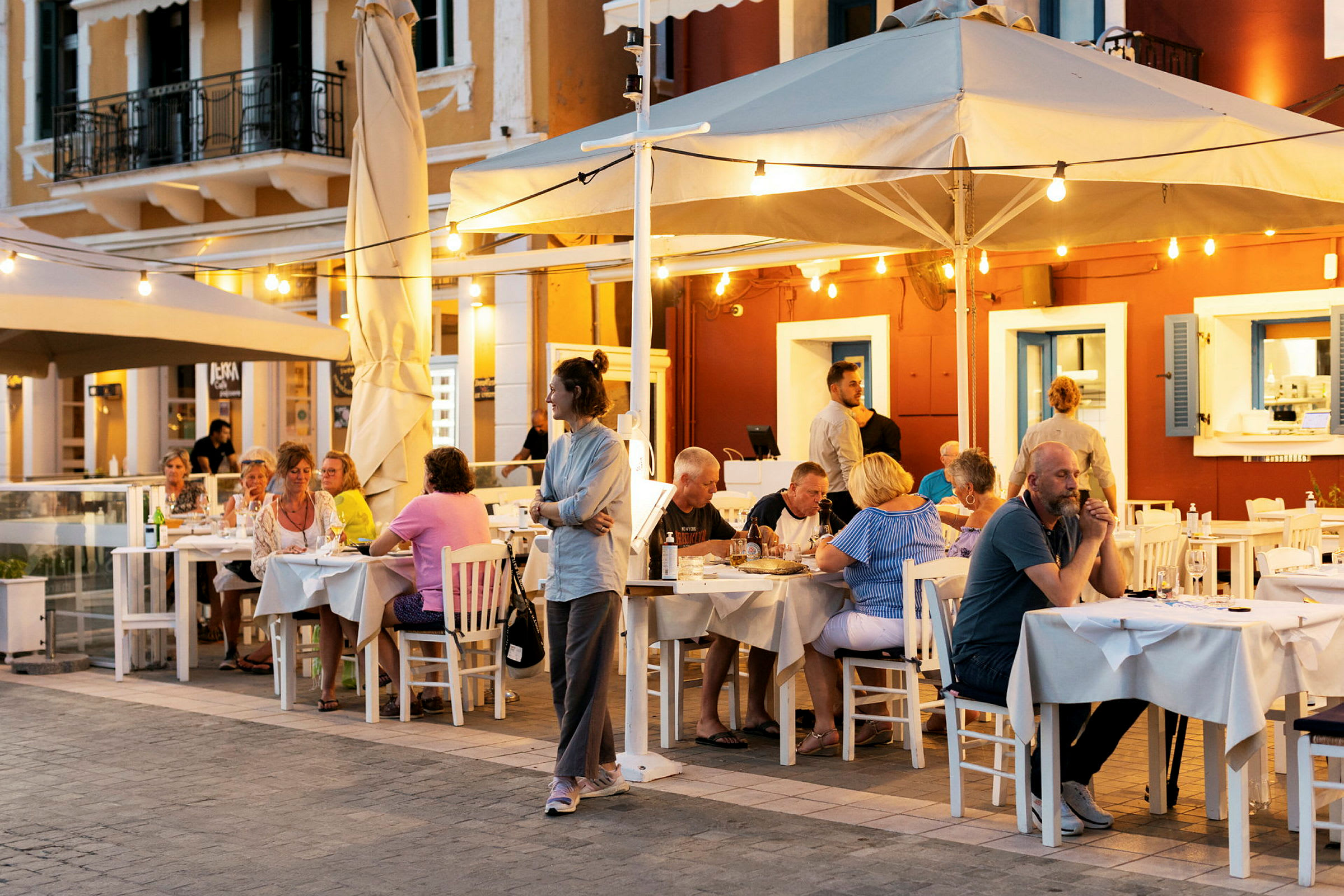 Utomhusrestaurang med gäster sittande vid bord under kvällstid. (AI-genererad text)