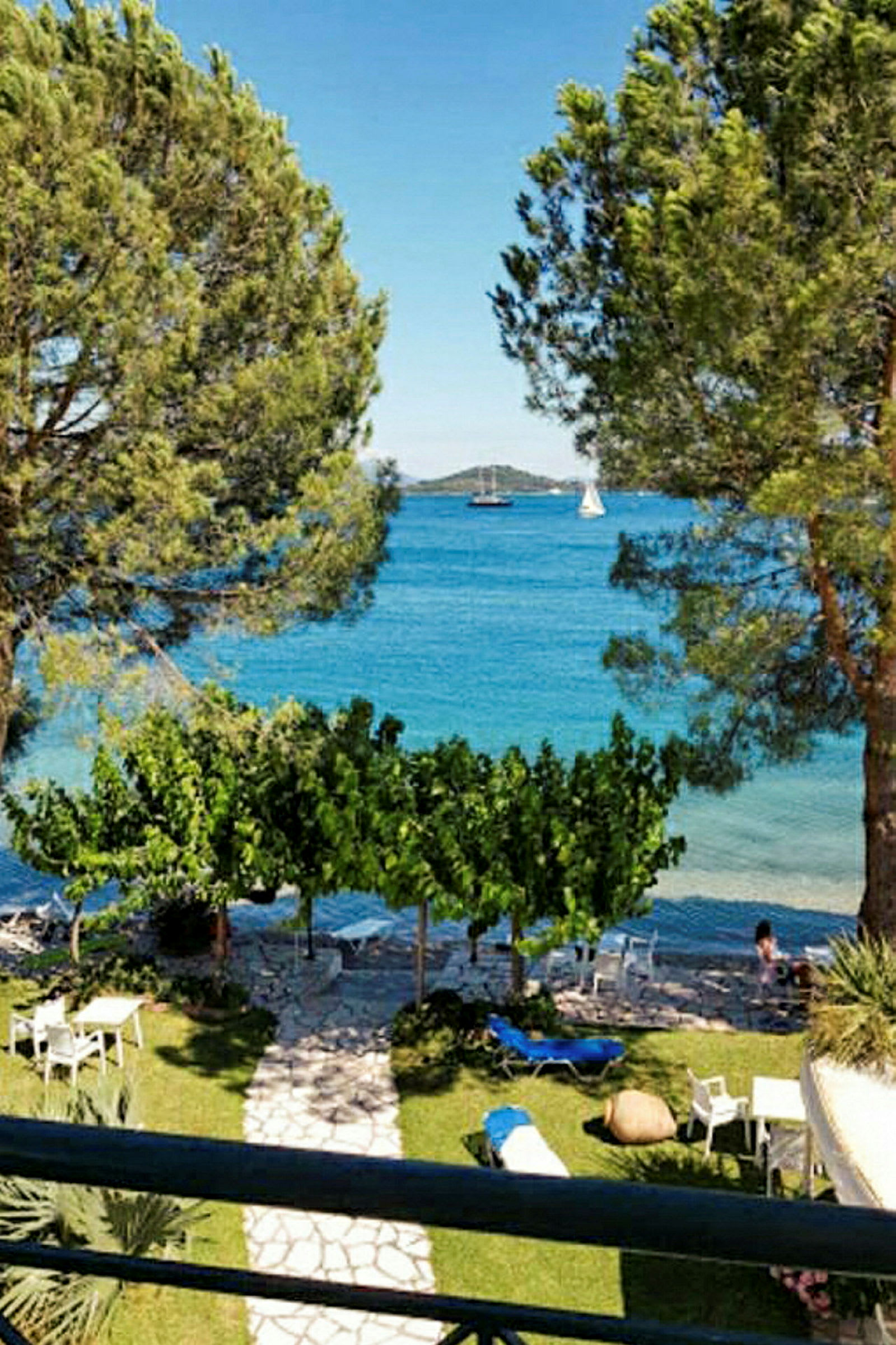 Vy från en terrass med träd, gräsmatta, stolar och bord, och havet i bakgrunden. (AI-genererad text)